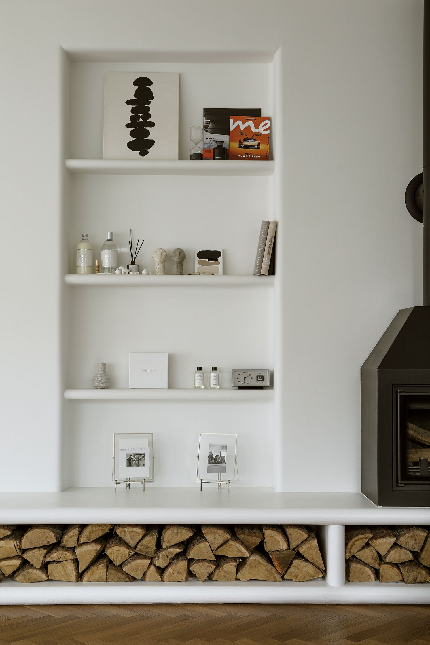 A modern living room with a long, multi-functional unit that integrates the firewood storage while doubling as seating. A built-in shelving niche and fireplace finish the living room space.