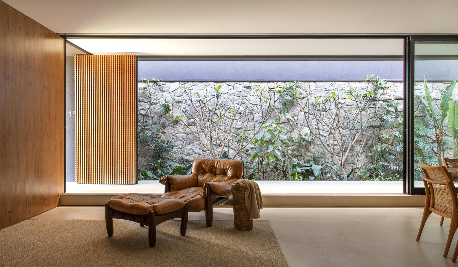 Glass walls and built-in freijó wood shelves connect living and dining areas with natural light and warmth.