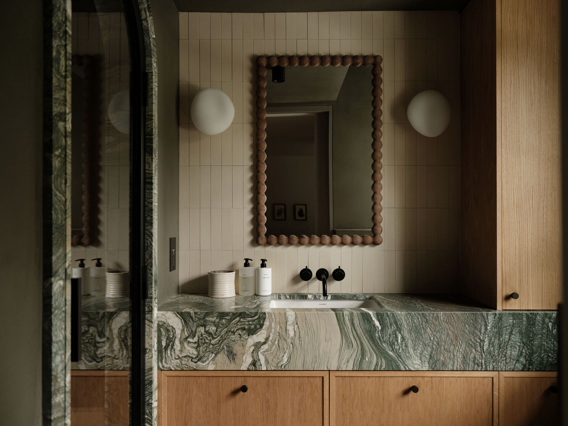 In this ensuite bathroom, a marble vanity with strong natural veining anchors the room, paired with timber cabinetry and vertically laid tiles that add subtle rhythm to the walls.