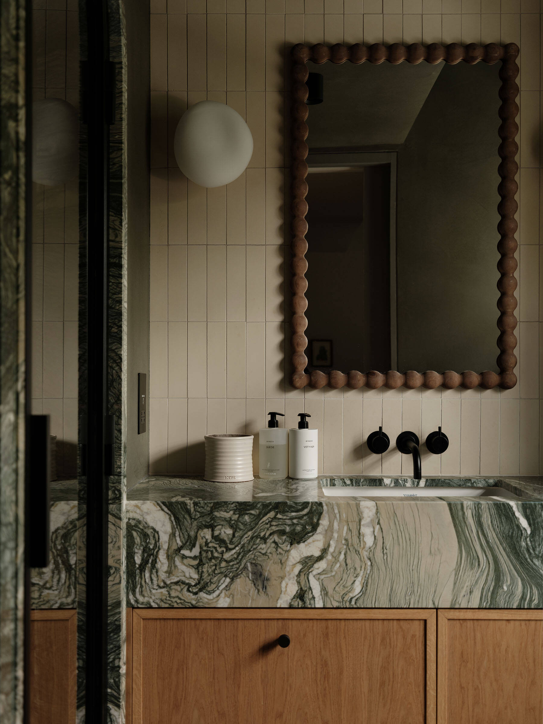 In this ensuite bathroom, a marble vanity with strong natural veining anchors the room, paired with timber cabinetry and vertically laid tiles that add subtle rhythm to the walls.