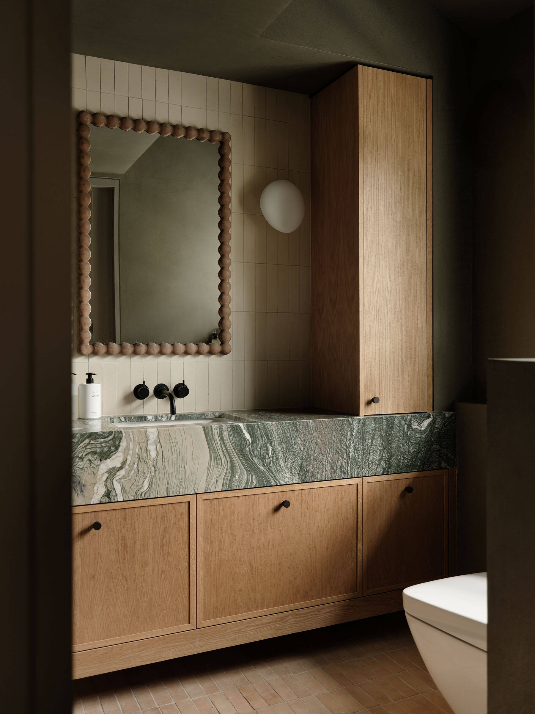 In this ensuite bathroom, a marble vanity with strong natural veining anchors the room, paired with timber cabinetry and vertically laid tiles that add subtle rhythm to the walls.