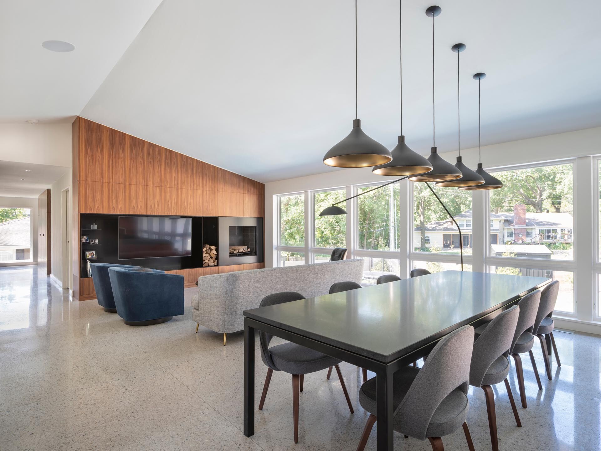 An open-plan living space connects the kitchen, dining area, and living room, with a dark dining table subtly defining the spaces while maintaining a bright and connected layout.