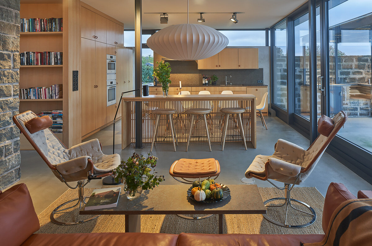 An open-plan living space with kitchen, dining, and bar area flows directly onto a terrace with water views and full-height glass doors.