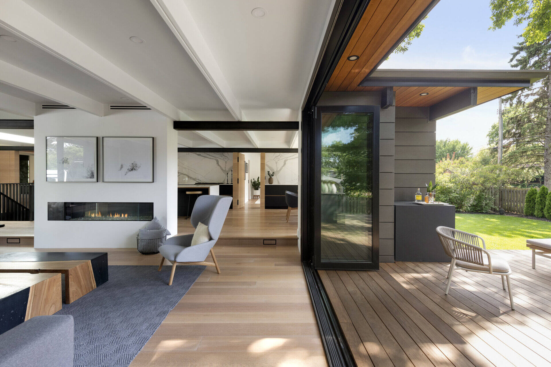 Las paredes de vidrio plegables desdibujan la línea entre el interior y el exterior, abriendo la sala de estar a una terraza de madera que extiende el espacio habitable hacia el patio. Una conexión perfecta con la naturaleza es un sello distintivo del diseño moderno de mediados de siglo.