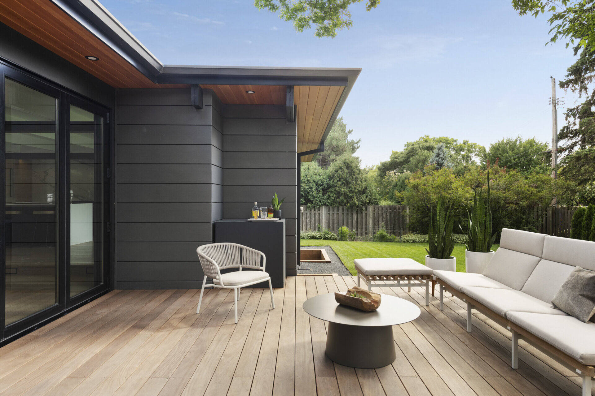 Las paredes de vidrio plegables desdibujan la línea entre el interior y el exterior, abriendo la sala de estar a una terraza de madera que extiende el espacio habitable hacia el patio. Una conexión perfecta con la naturaleza es un sello distintivo del diseño moderno de mediados de siglo.