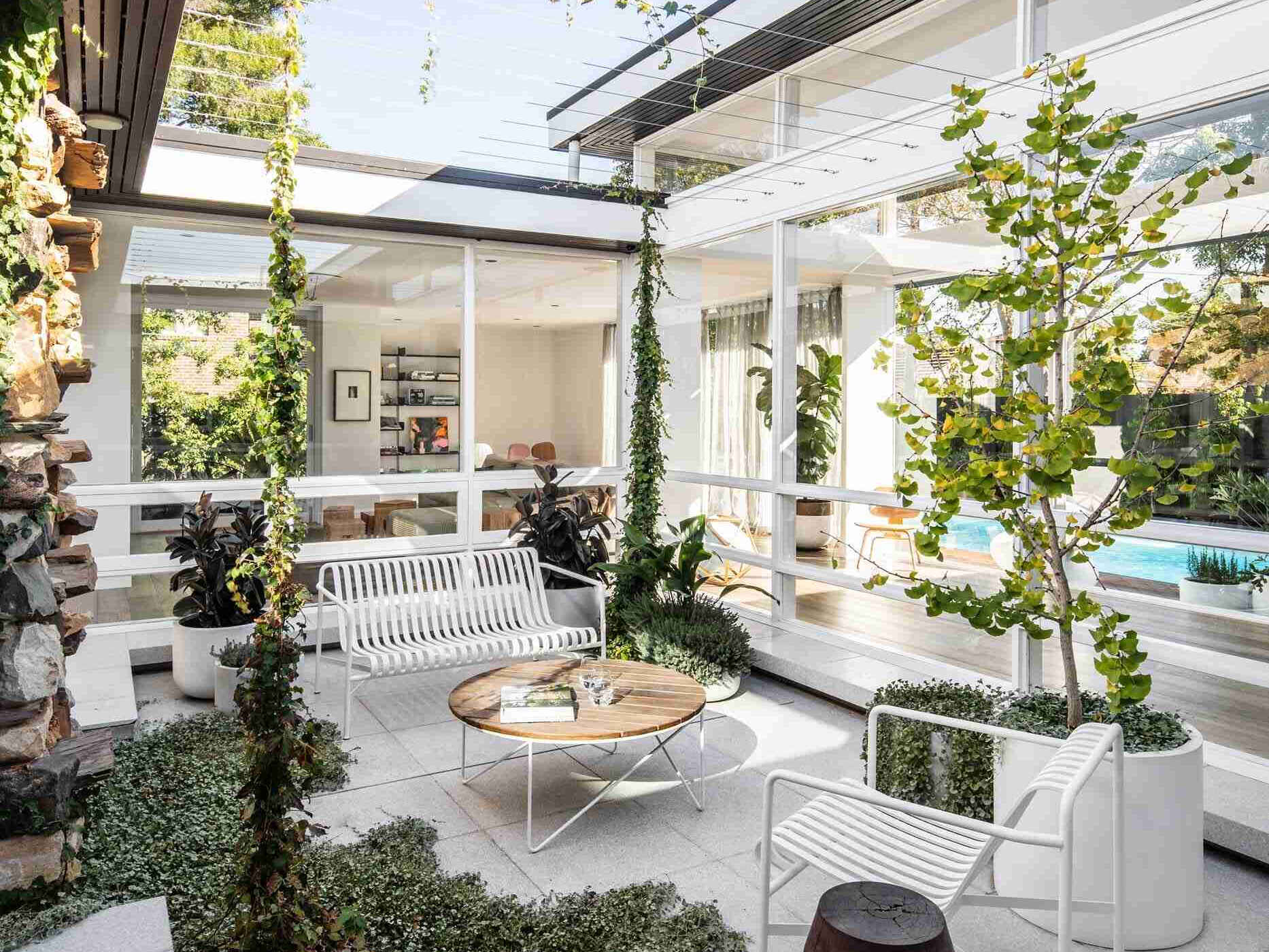 A bright courtyard sits at the center of this renovated mid-century home, surrounded by white walls, simple furniture, and planters that will eventually be shaded by vines.