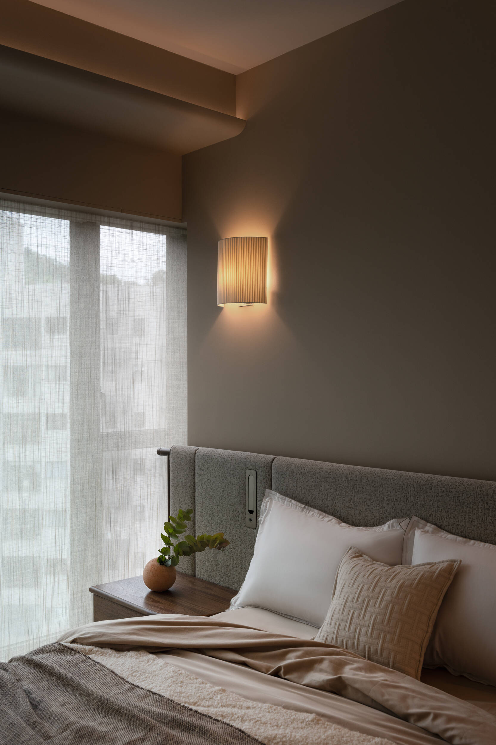 In the primary bedroom, soft textures, filtered light, and a custom fabric headboard create a calm, cocoon-like retreat.