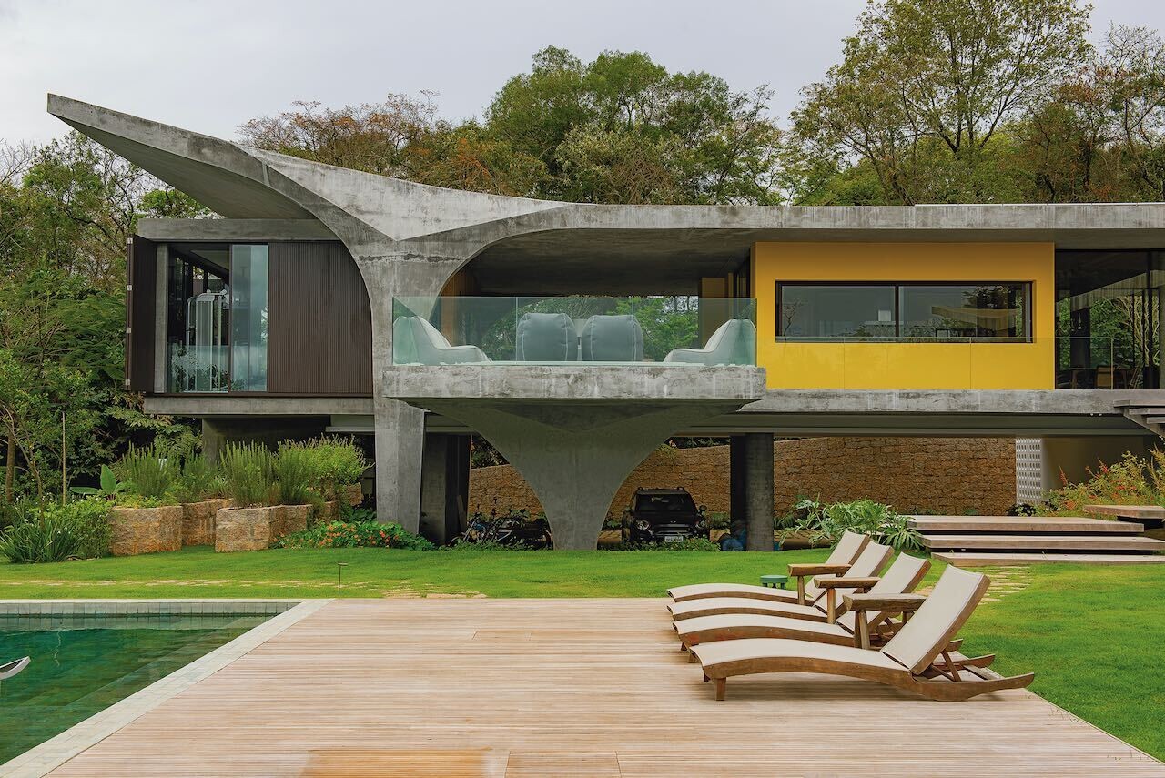 A modern concrete home designed to appear as if it floats above a sloped, tree-filled site, with sculptural pillars defining its bold architectural form.