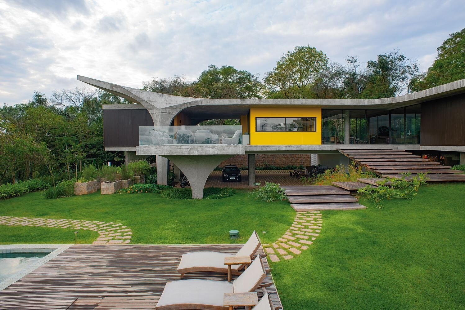 An expansive concrete balcony with wood stairs leading to outdoor spaces, extending the home across multiple levels.