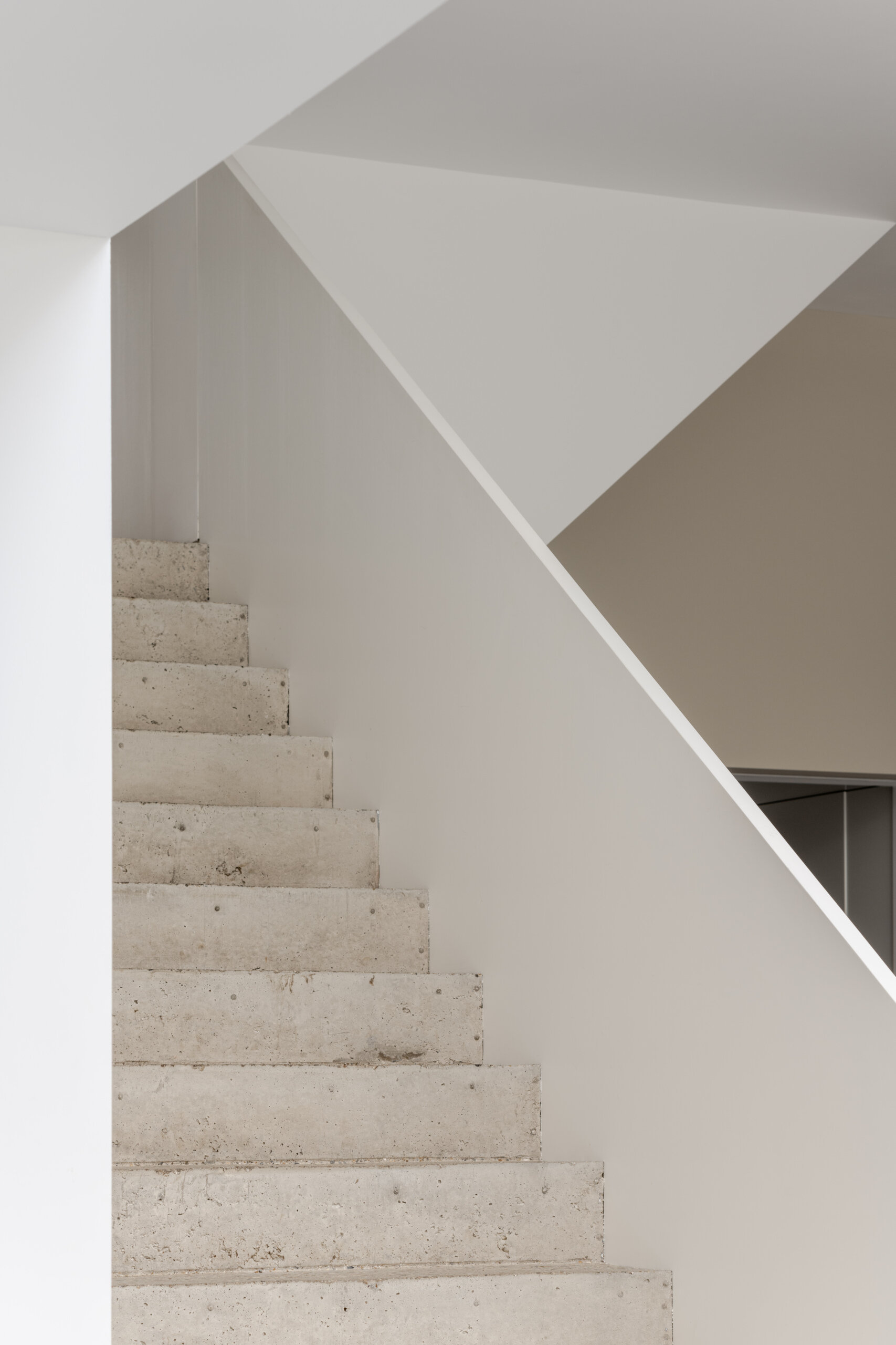 The main staircase is constructed from concrete using reclaimed aggregate from demolition waste, connecting the home’s tiered layout while supporting the project’s sustainability goals.