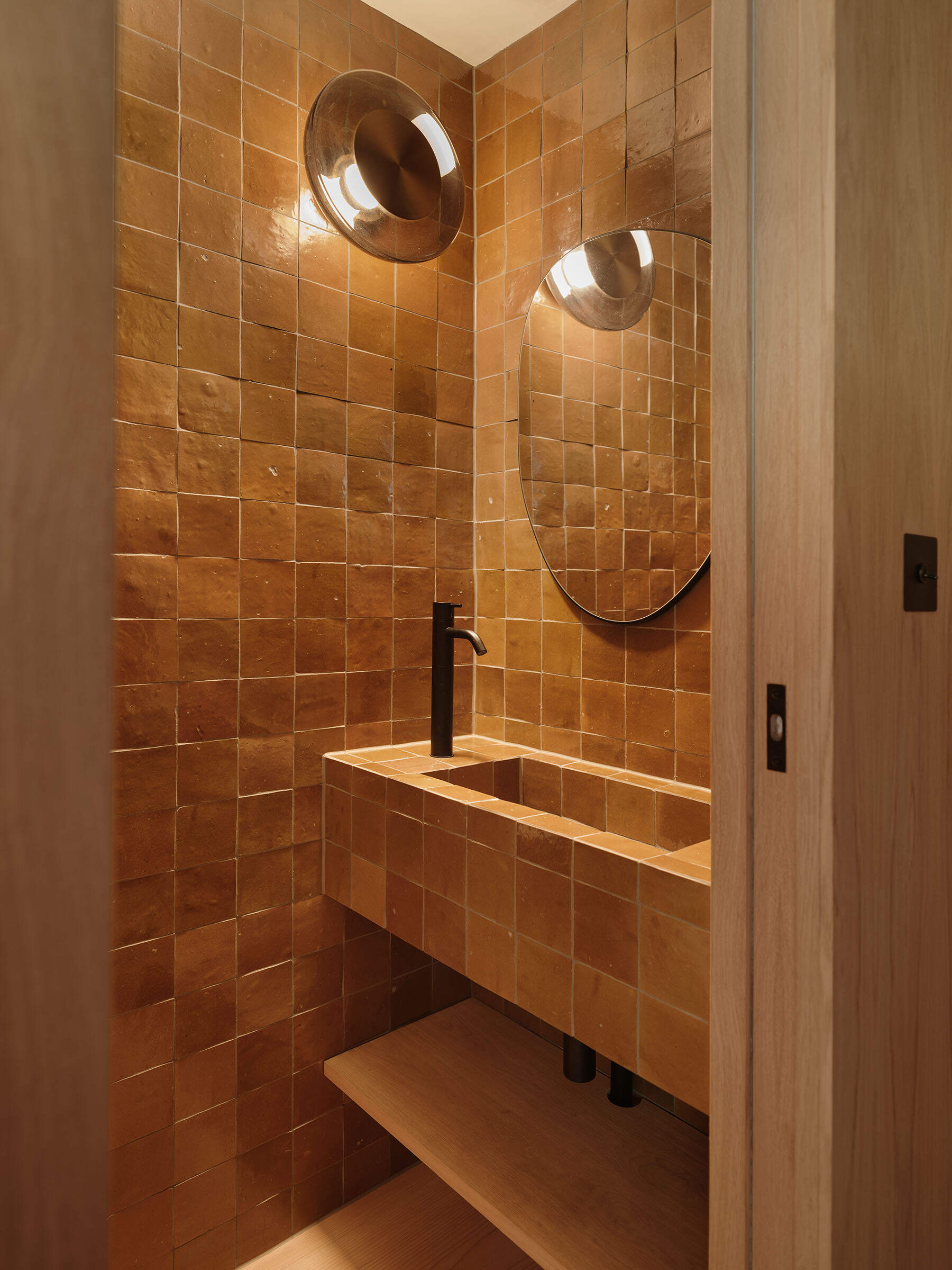 A ground floor powder room was introduced as part of the new layout. Wrapped entirely in small-format square tiles, the space feels warm and grounded, with subtle variations in tone adding depth across the walls and integrated sink.