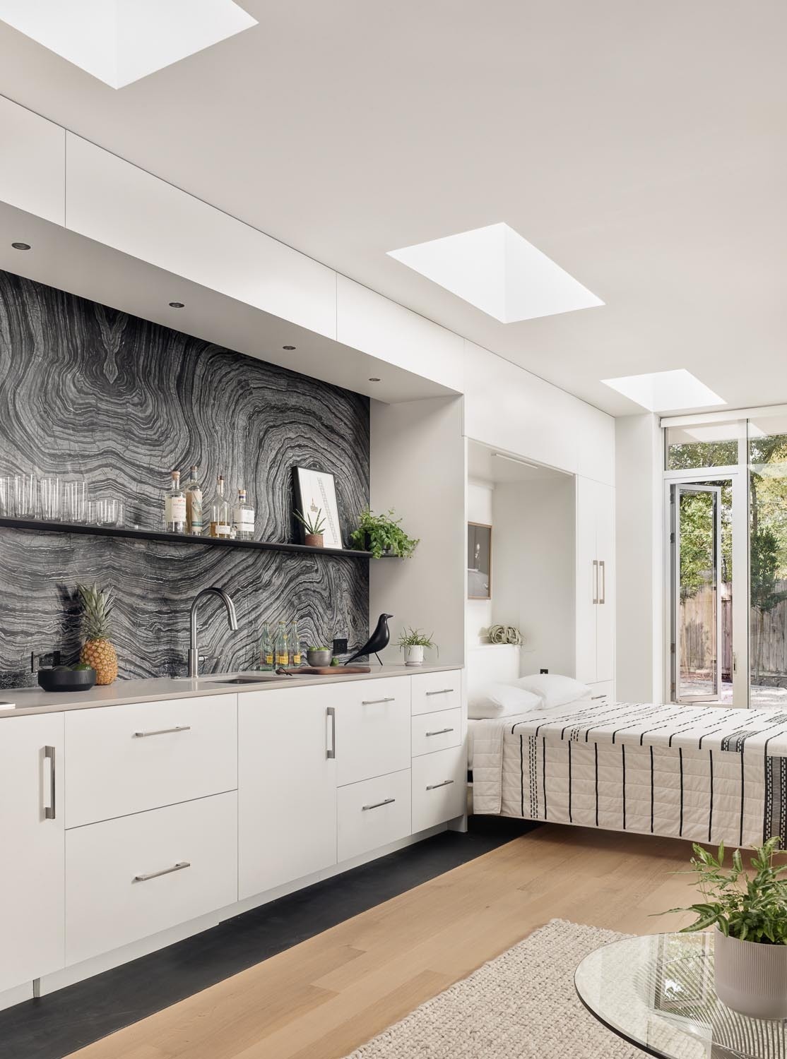 This small kitchen inside a 540 square foot Austin ADU features white cabinets, skylights, Kenya Black marble backsplash slabs, and compact appliances for a clean modern look.