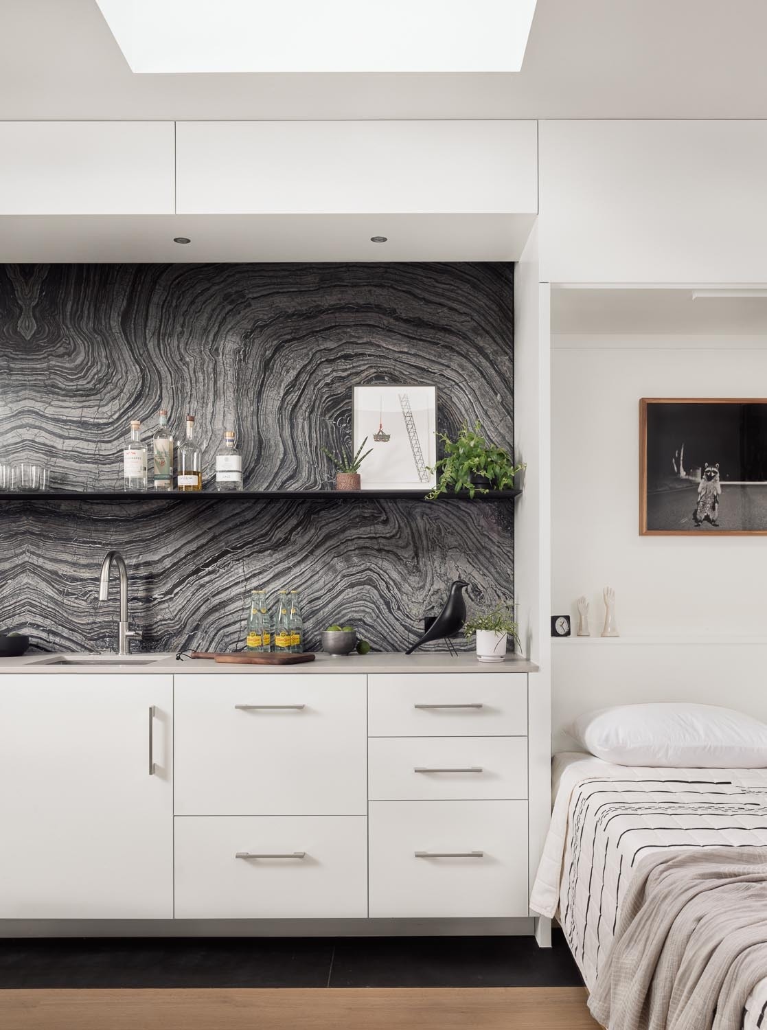 This small kitchen inside a 540 square foot Austin ADU features white cabinets, skylights, Kenya Black marble backsplash slabs, and compact appliances for a clean modern look.