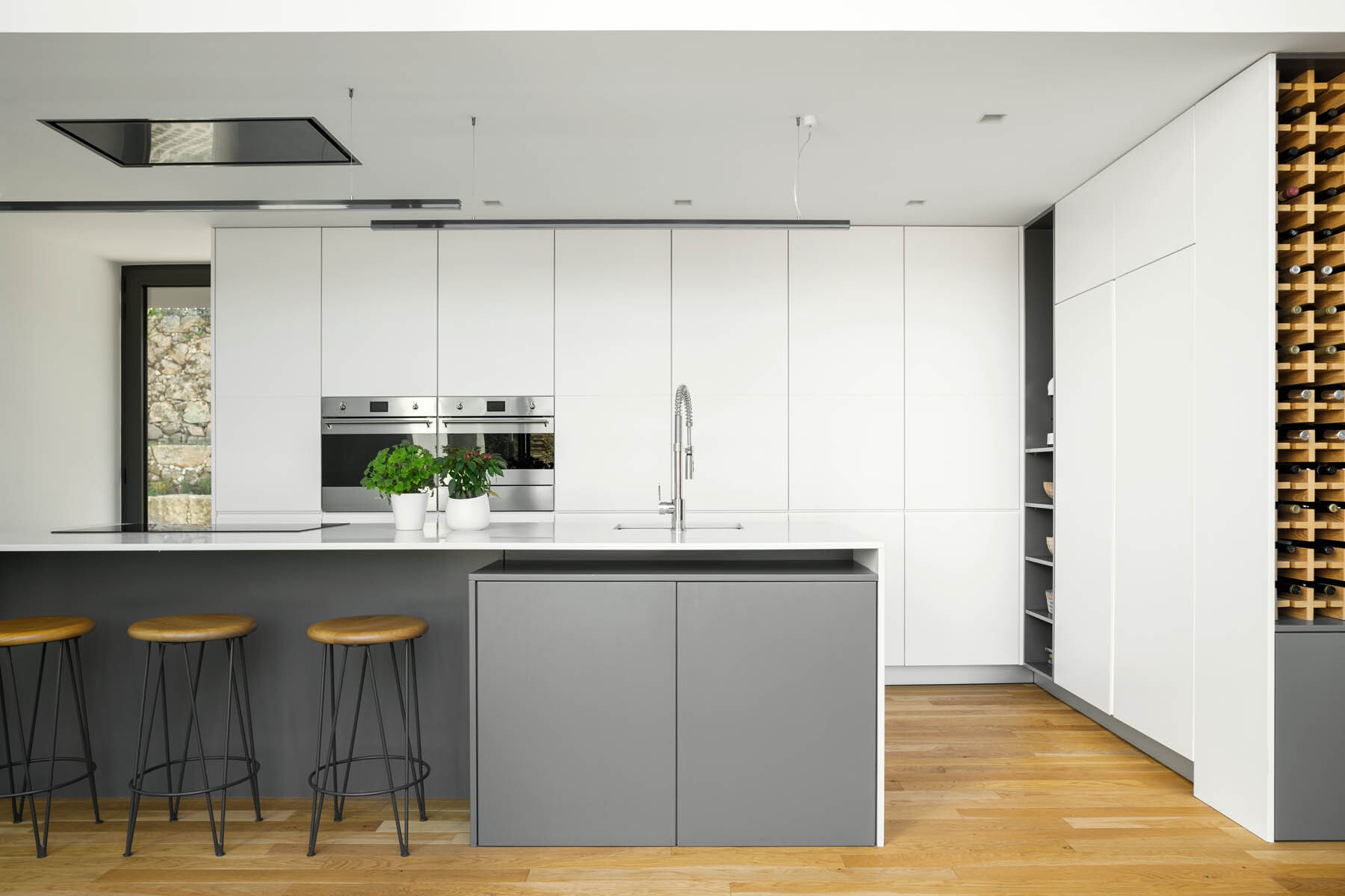 A minimalist kitchen pairs white cabinetry with a gray island and built-in wine storage for a clean and practical design.