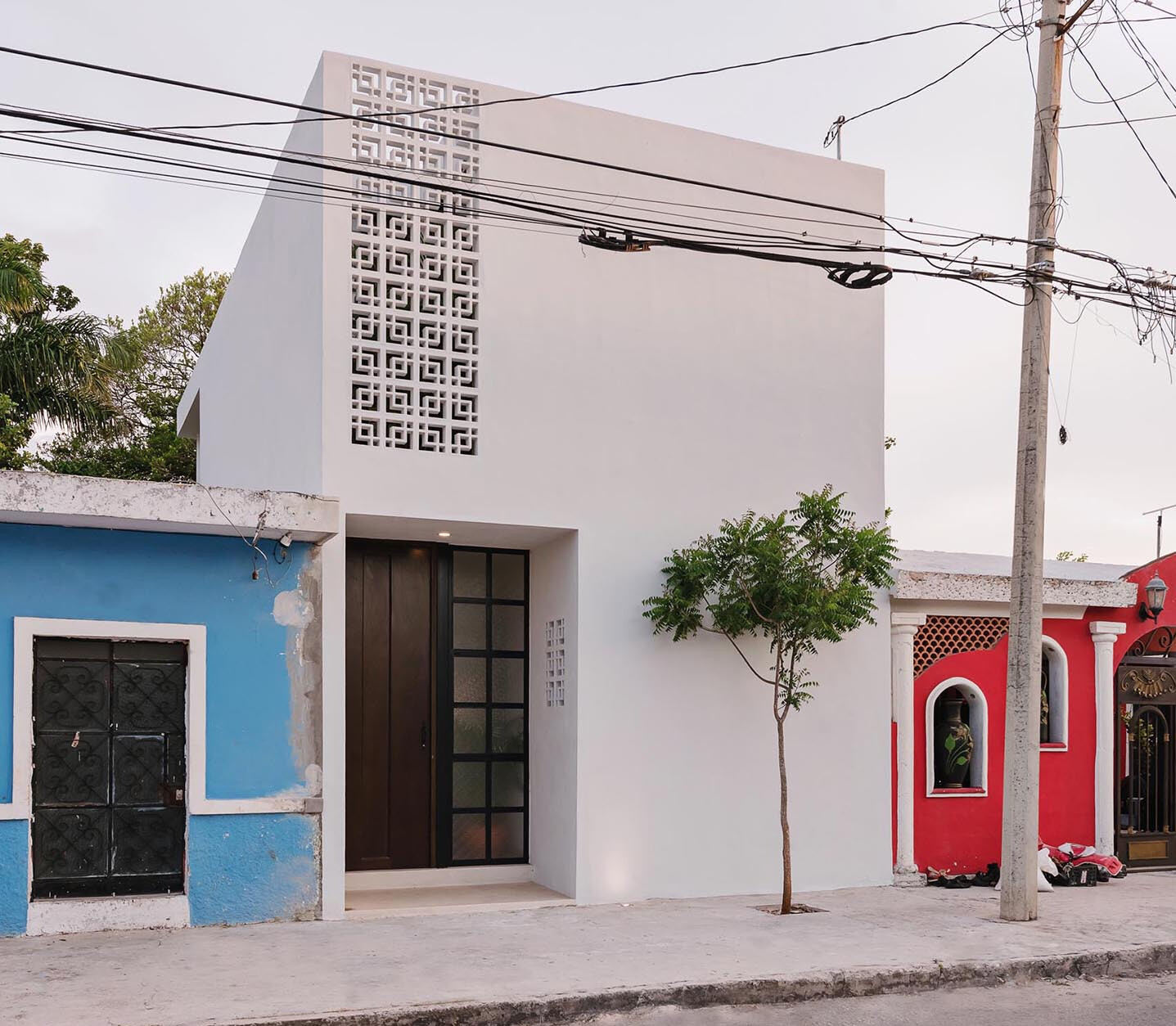 A compact modern home that reveals far more than its calm white exterior suggests. From the street, the house presents a restrained presence, but stepping inside reveals a layered sequence of spaces filled with greenery, light, and carefully framed views.