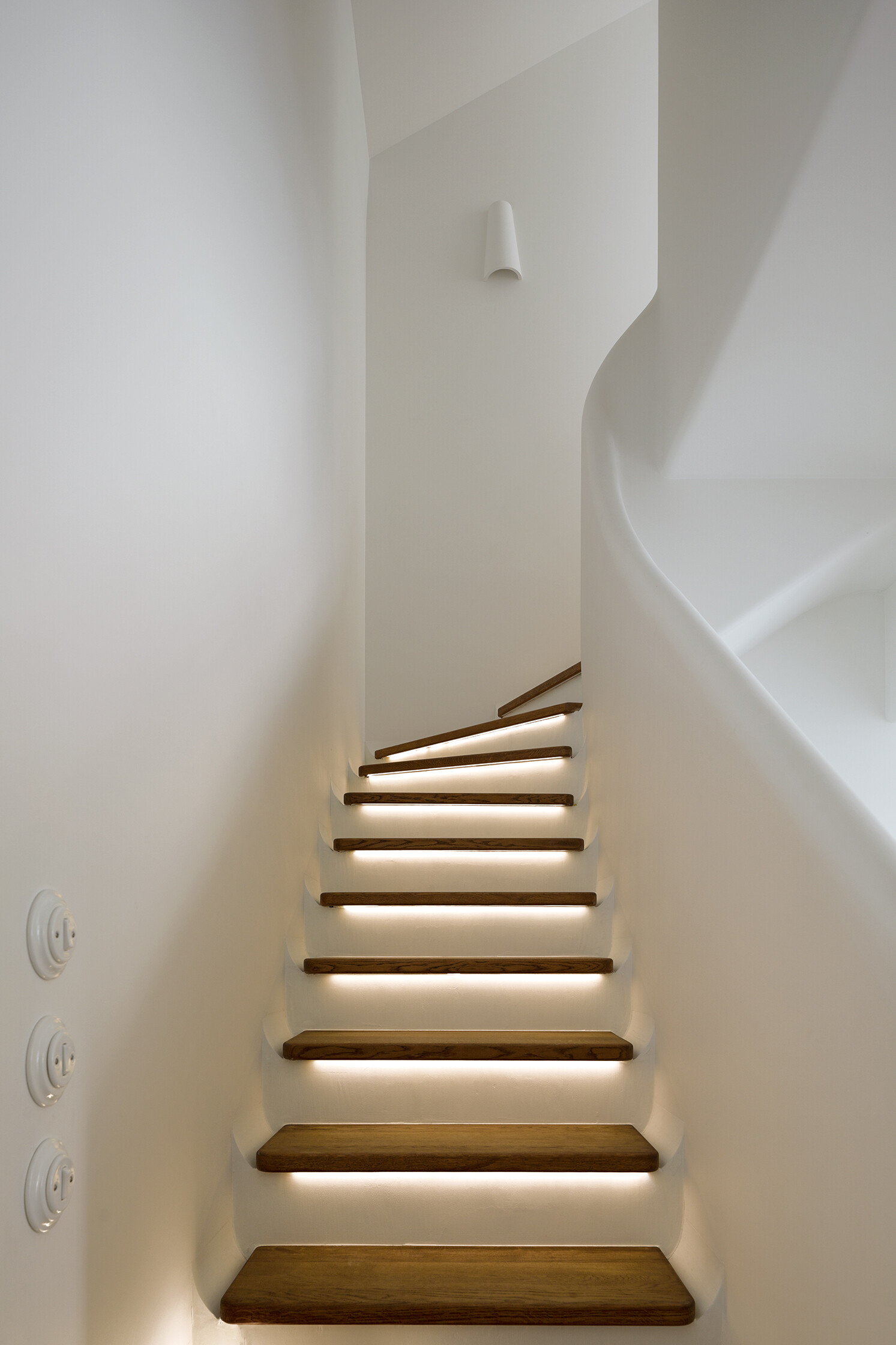 A sculptural staircase with wood treads and a flowing silhouette that anchors the home while connecting each space.