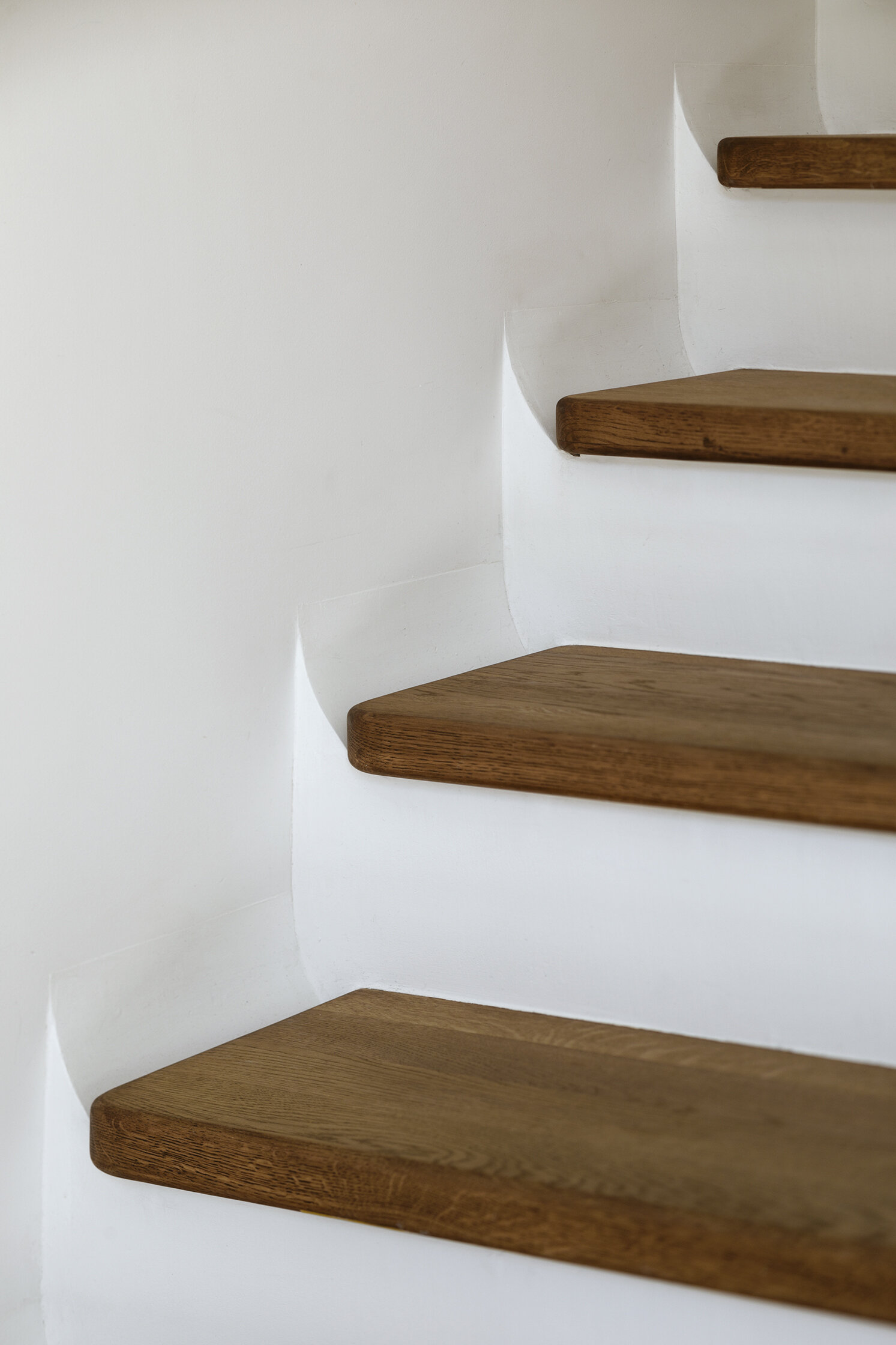 A sculptural staircase with wood treads and a flowing silhouette that anchors the home while connecting each space.