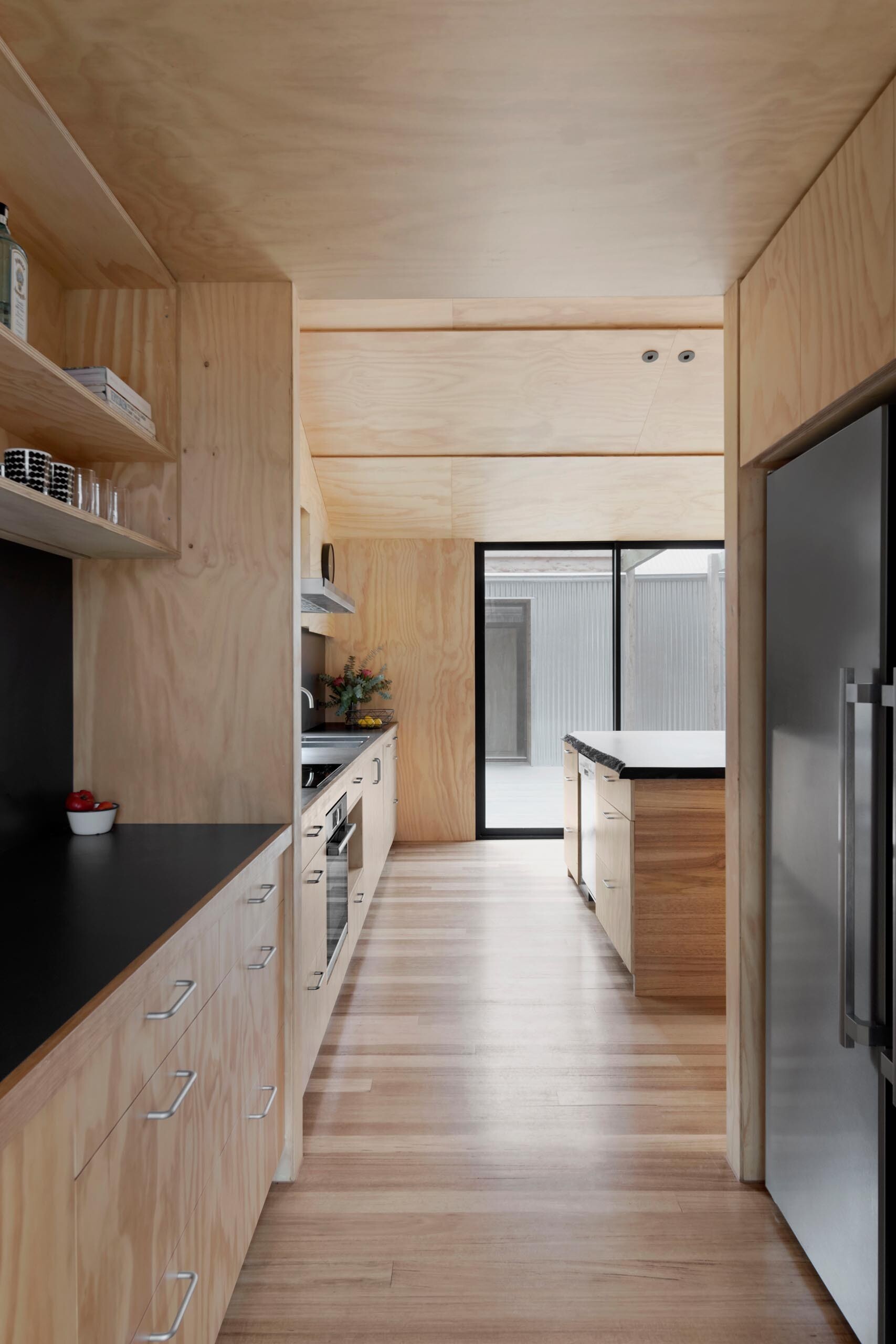 A modern kitchen combines timber and matte black finishes, with a live edge island and hidden fridge for a clean, functional layout.