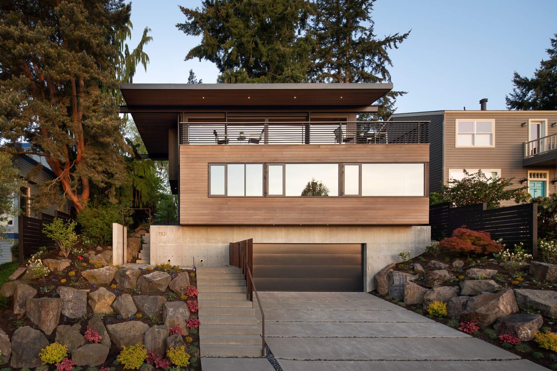 A modern Seattle facade with concrete, wood, and steel, softened by a garden approach and elevated entry sequence.
