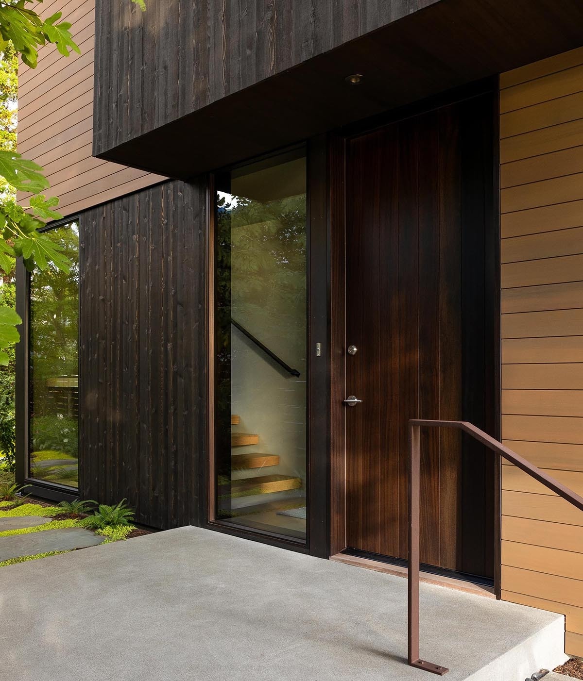 A modern Seattle facade with concrete, wood, and steel, softened by a garden approach and elevated entry sequence.