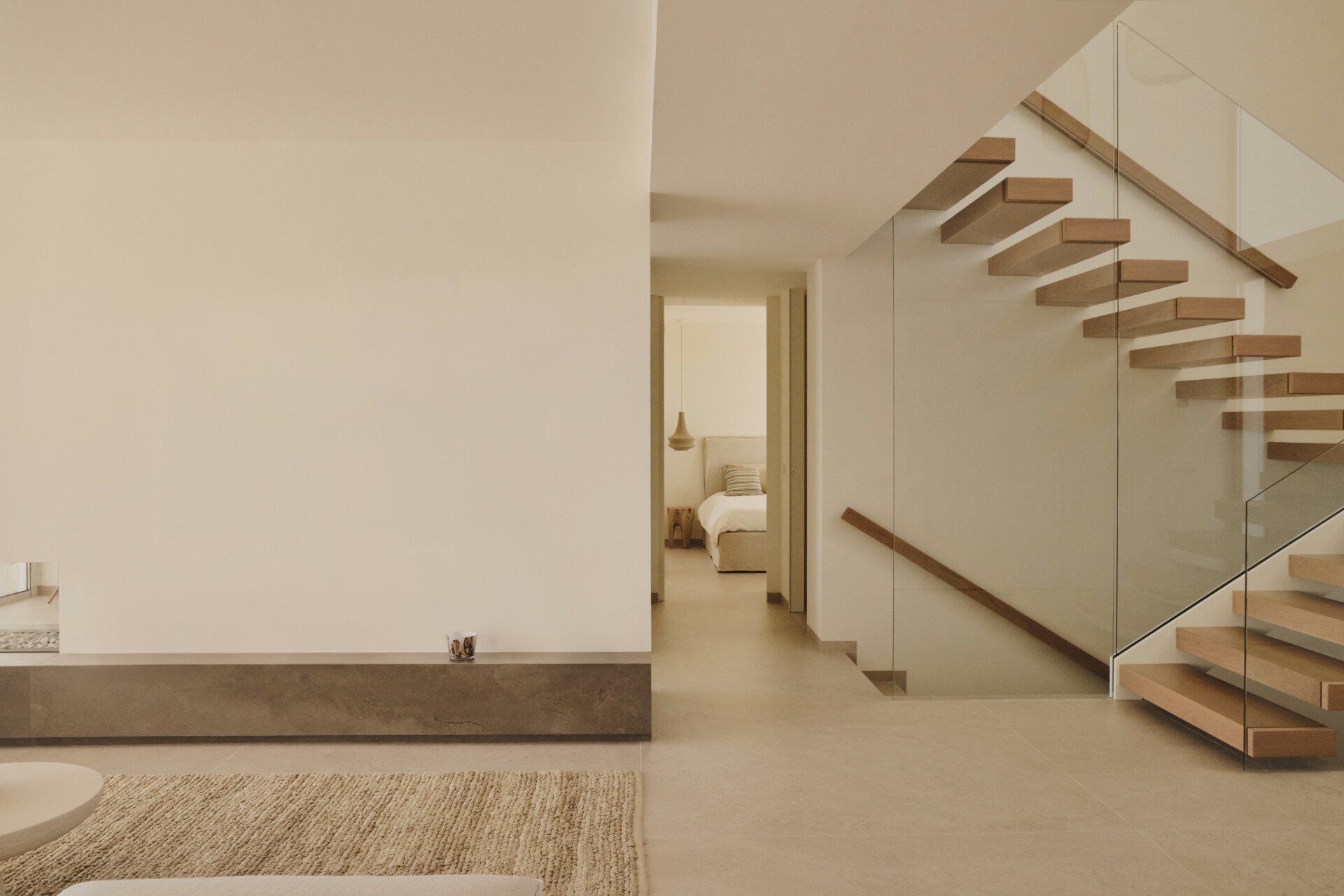 Back inside and by the entryway, a sculptural wood and glass staircase rises within a double height foyer, shaping the vertical experience of the interior.