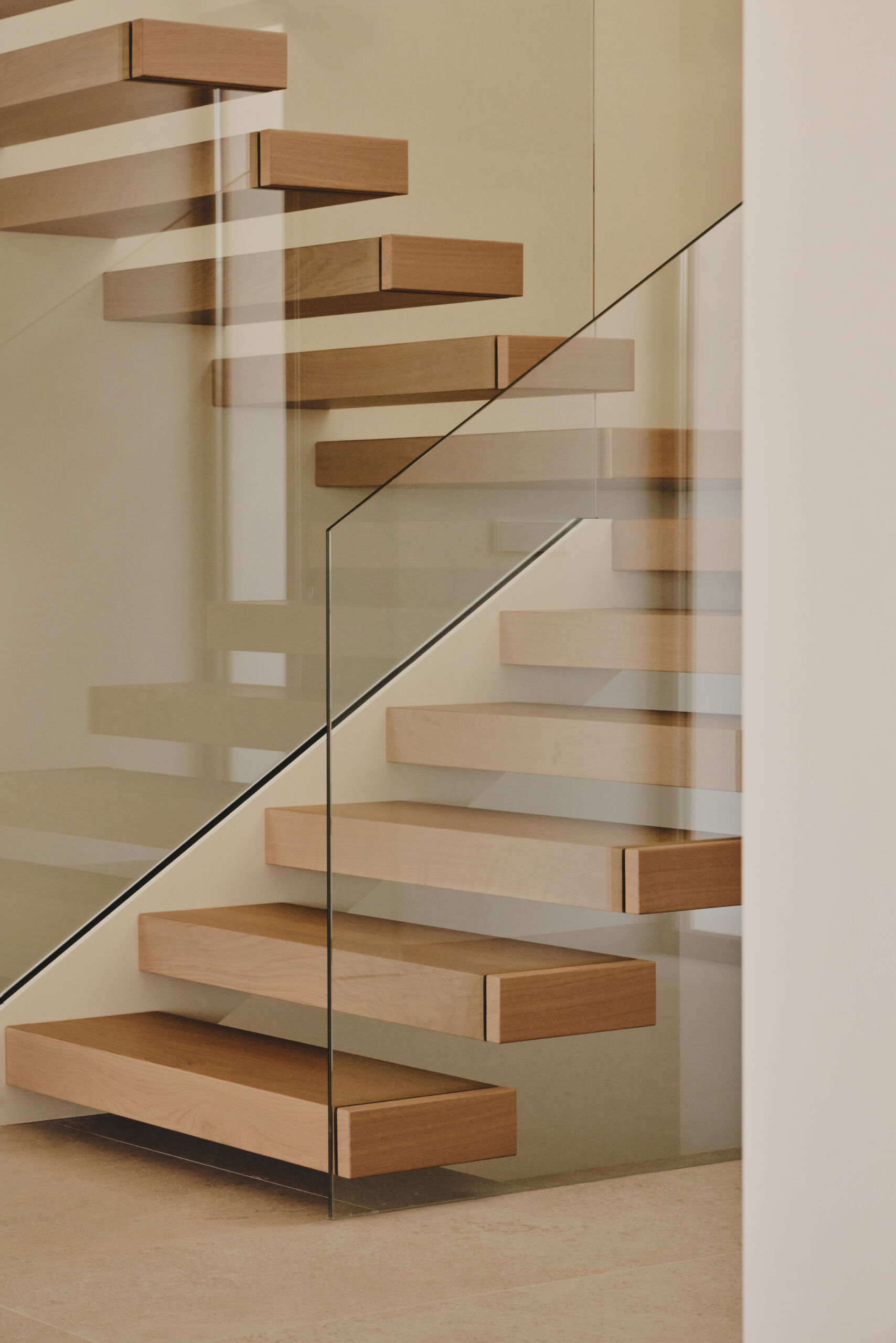 Back inside and by the entryway, a sculptural wood and glass staircase rises within a double height foyer, shaping the vertical experience of the interior.