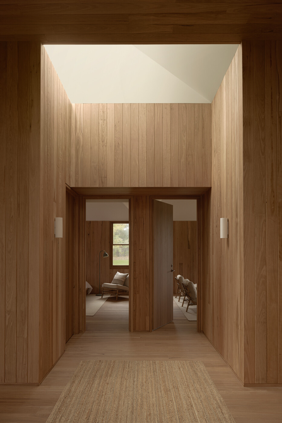 A timber-lined entry hall with skylights leads into a narrow linkway between the two pavilions, creating a sequence of shifting spaces throughout the house.
