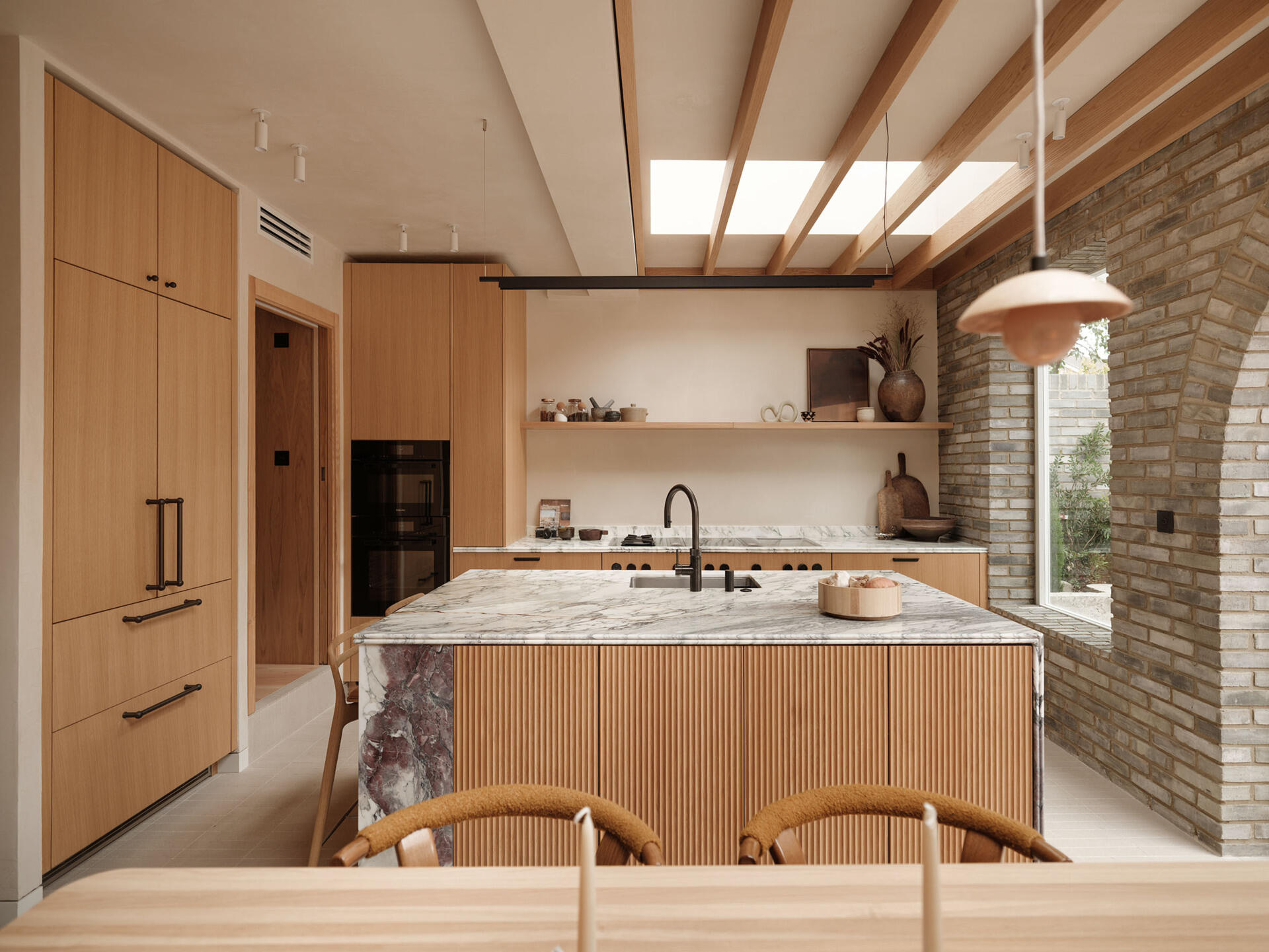 The kitchen is fully integrated into the overall layout rather than treated as a separate room. A consistent material palette of timber, stone, and plaster ensures visual continuity. This approach allows the kitchen to support both everyday routines and social use without feeling disconnected from the rest of the home.