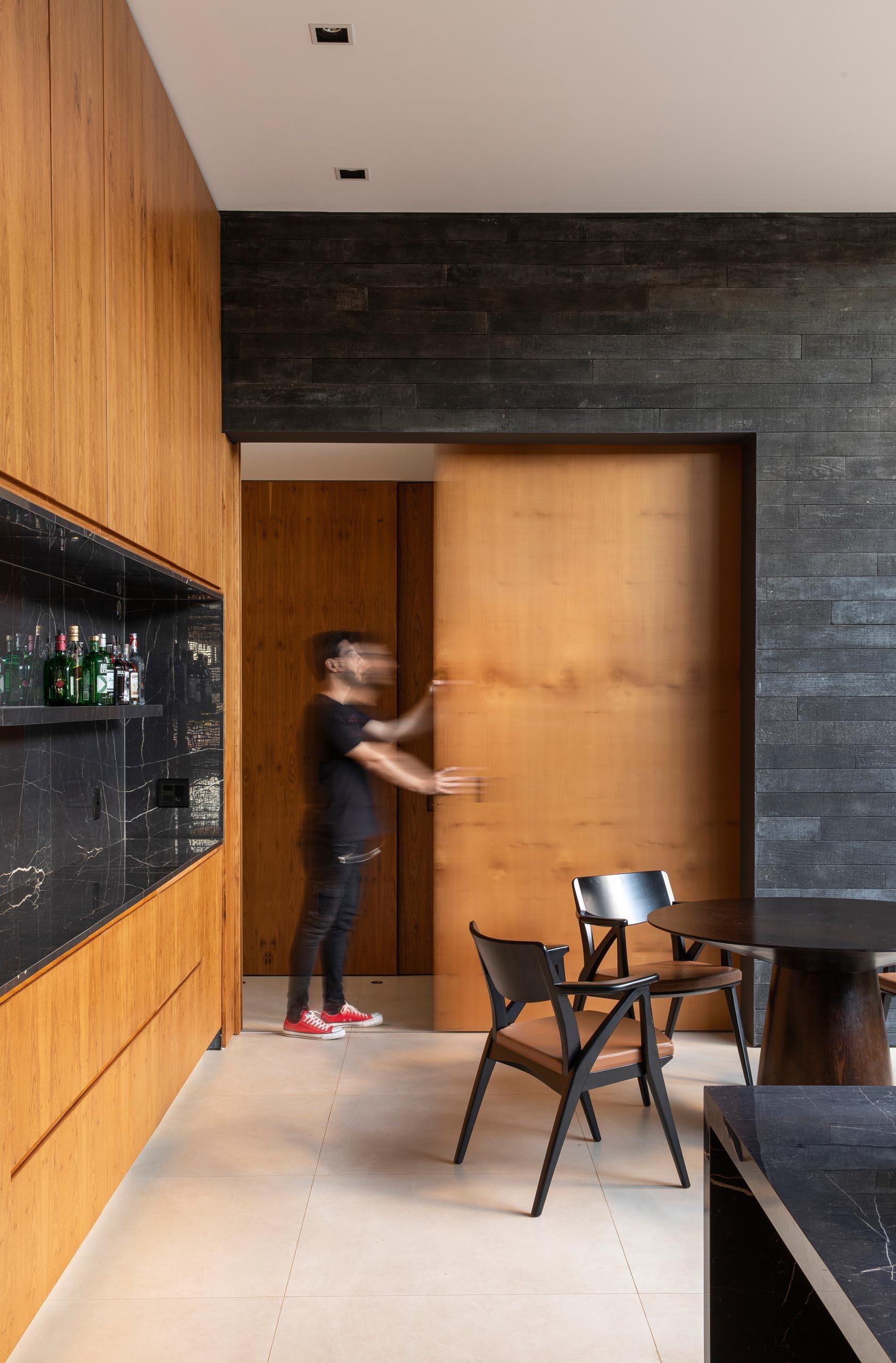 Wood cabinets meet black stone countertops and a floating shelf, with a sliding door offering privacy from the main living space.