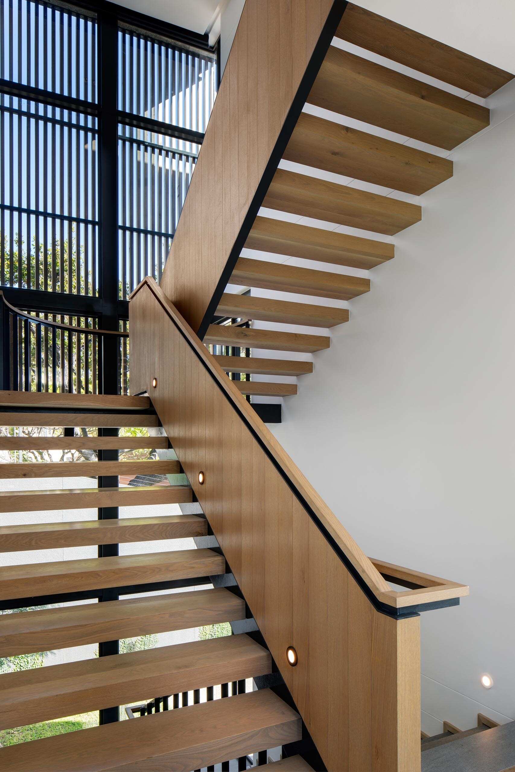 Una escalera de madera con detalles en negro conecta los distintos niveles de la casa y al mismo tiempo hace eco del diseño escalonado del edificio.