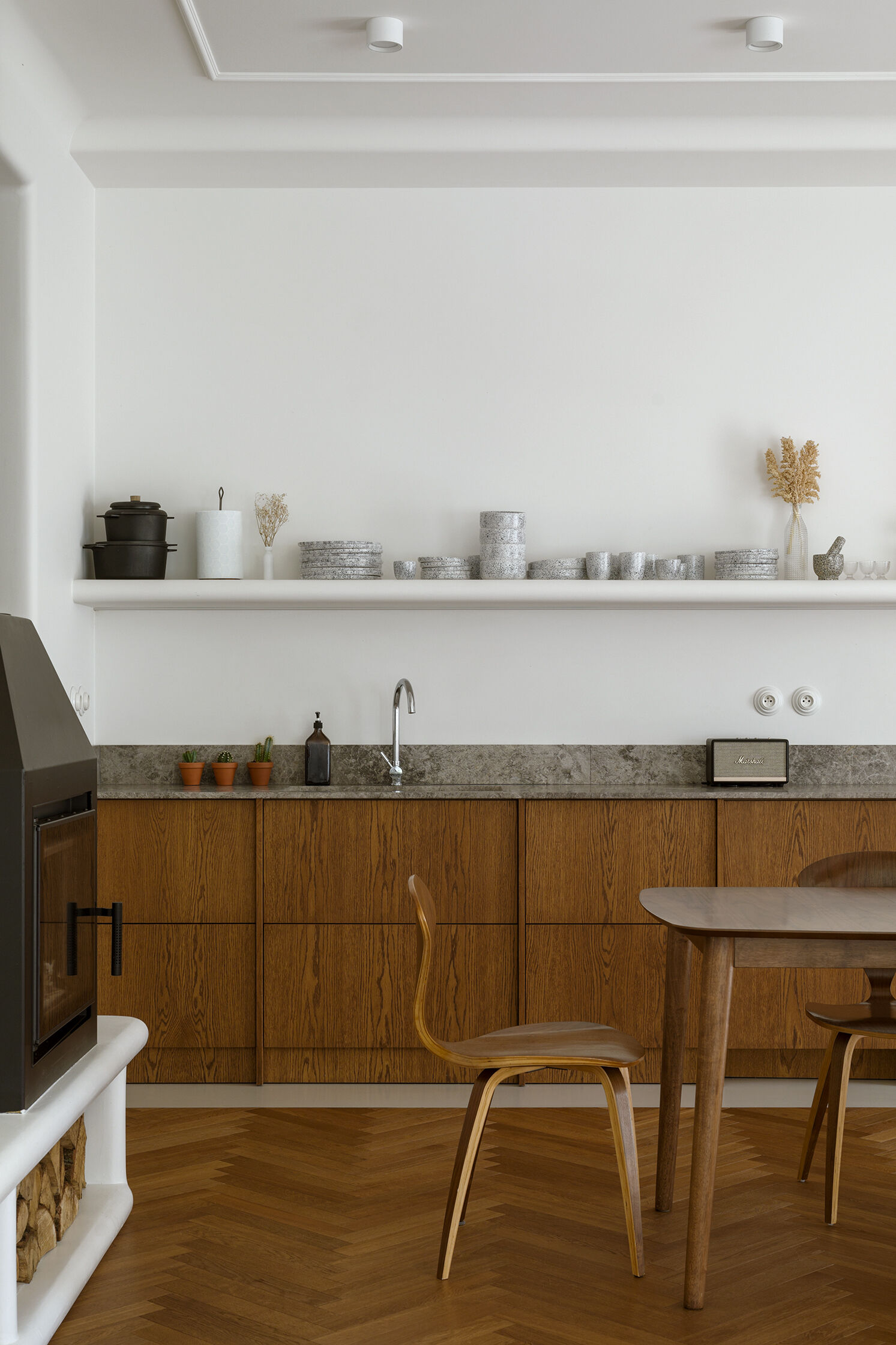 The dining room separates the kitchen from the living room. A concealed storage area keeps the space visually clean, allowing materials like the wood cabinets, and form to take focus. A shelf with a curved front creates a place to display kitchenware.