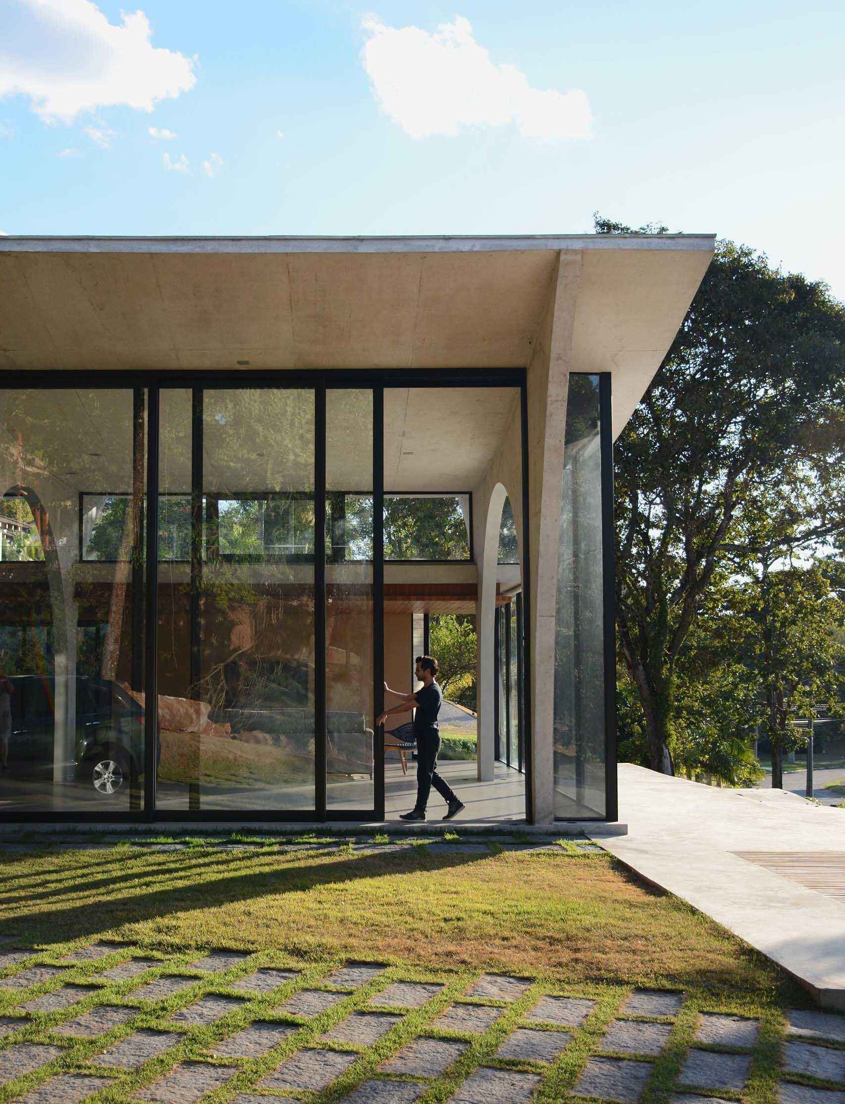 The living room, dining area, and kitchen share a dramatic double height space framed by concrete arches and large sliding glass doors that connect the interior to the gardens.