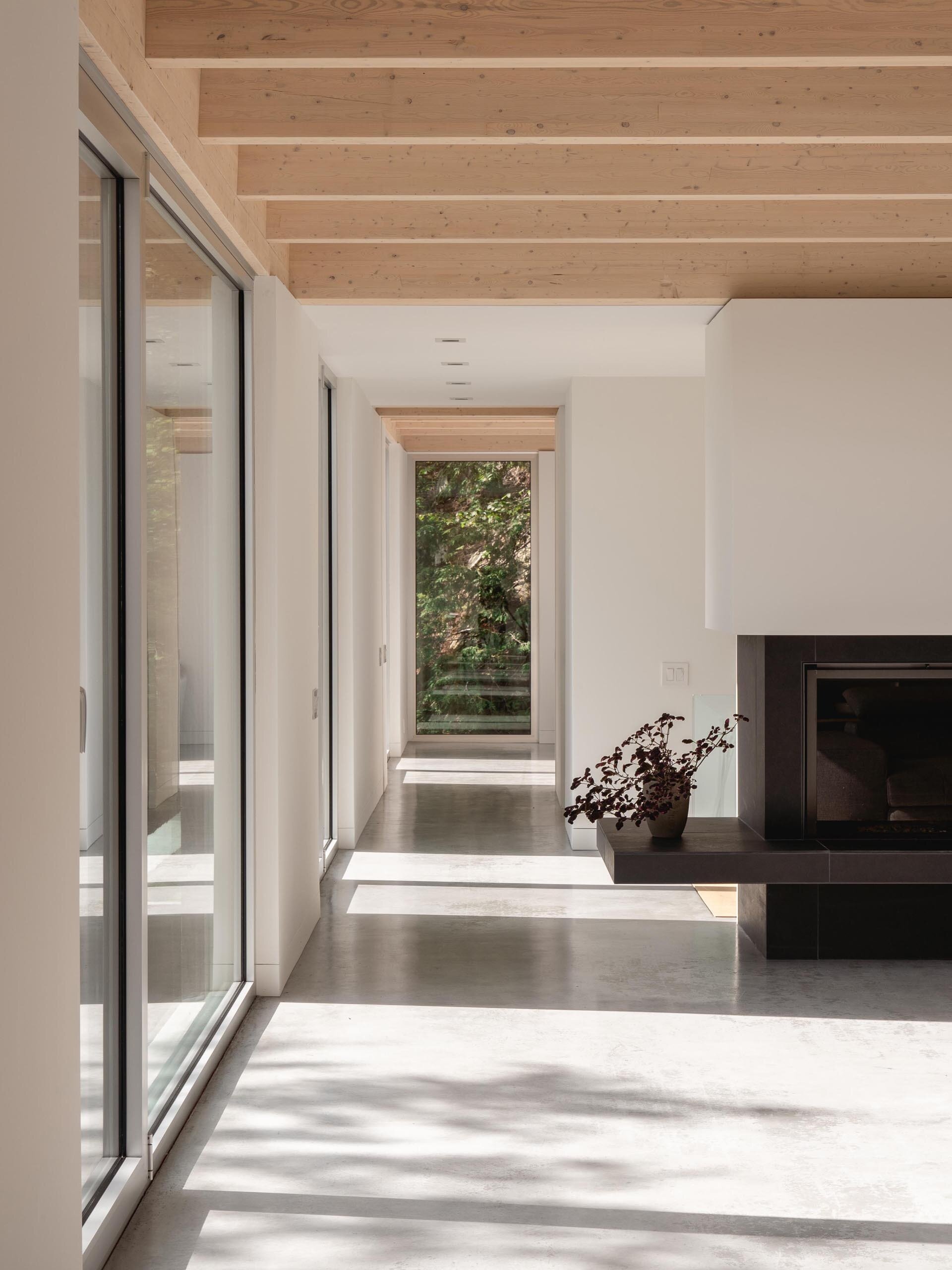 Los pisos de concreto, las paredes blancas y las ventanas de aluminio natural crean una paleta interior relajante que complementa los acabados de madera de la casa.