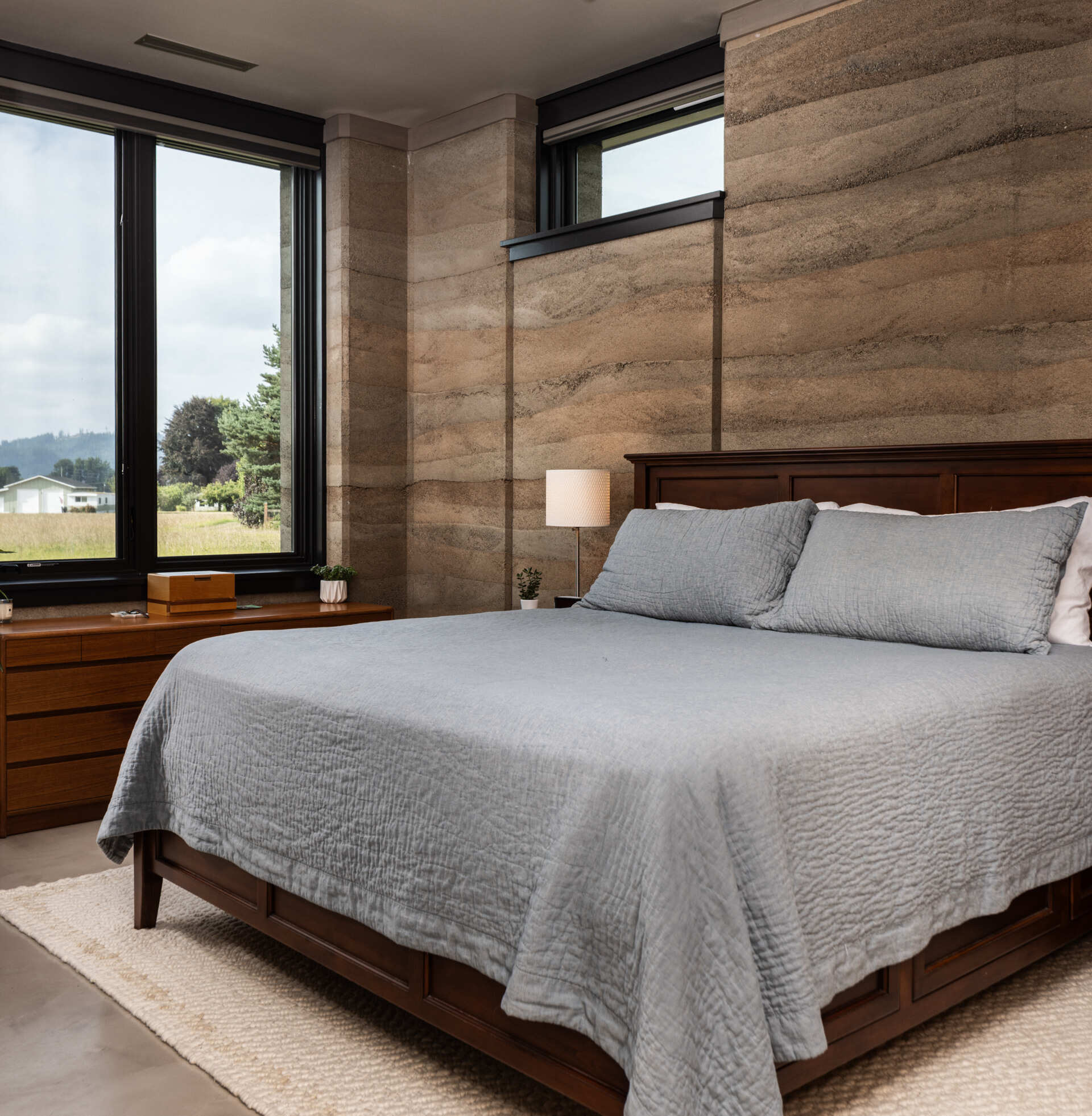 In the bedroom, the wood furnishings complement the natural aesthetic and color of the walls, while the windows allow for views and light.