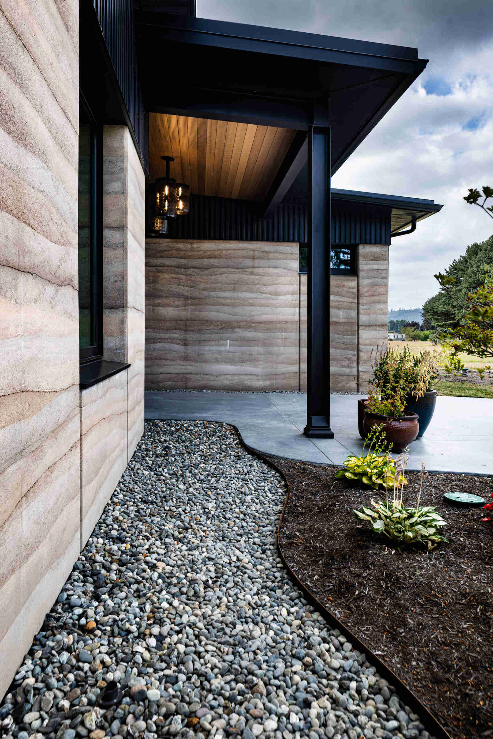 The entryway introduces the home’s natural materials with exposed rammed earth and washed rock, creating a grounded connection between the house and the surrounding farmland.
