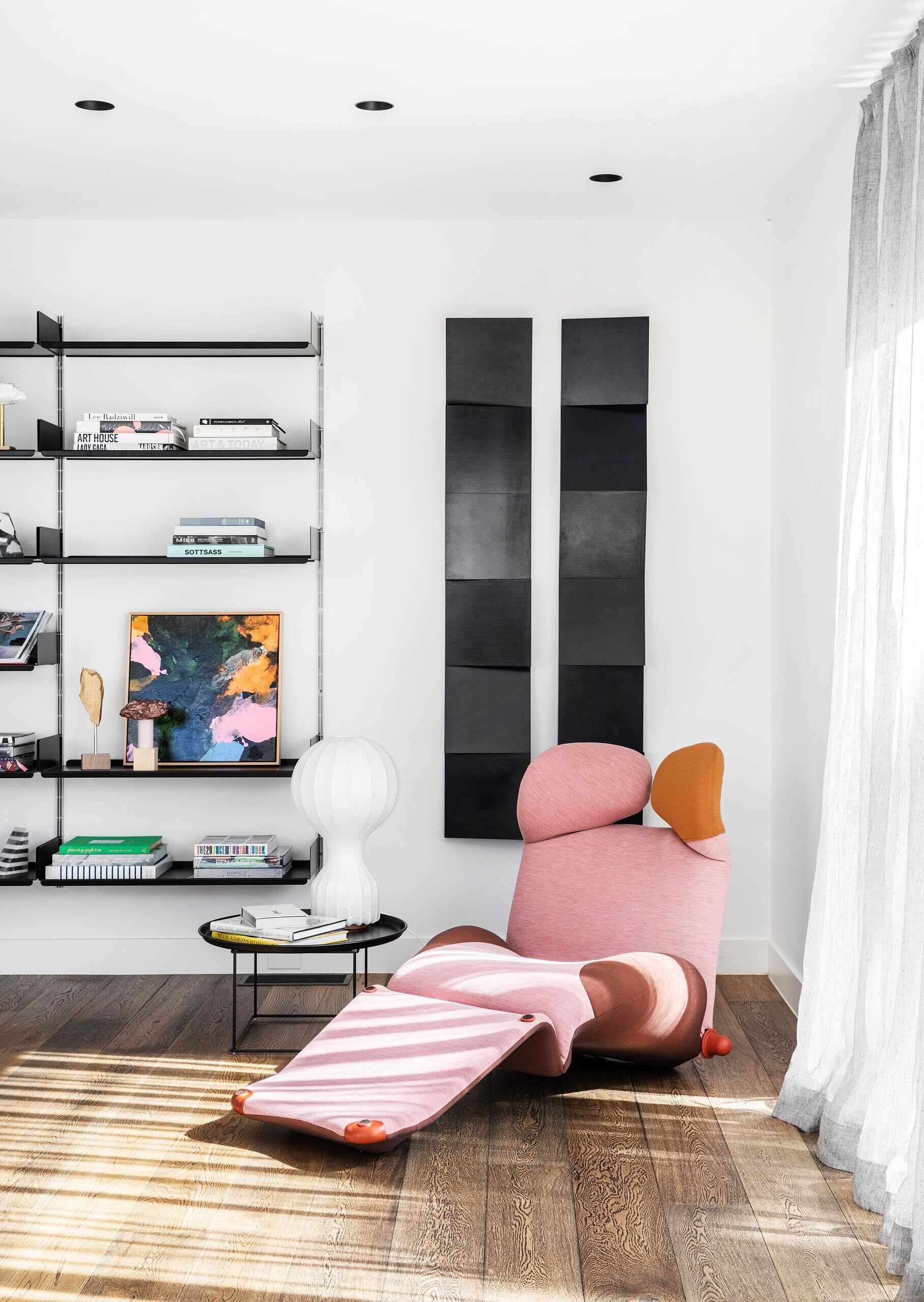 A sculptural pink chaise and wall-mounted bookshelf create a compact reading nook tucked behind the living room.