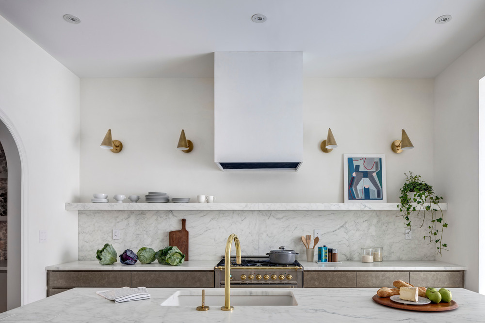 A marble island stretches across the width of this Brooklyn townhouse kitchen, designed for social cooking and framed by steel doors that open to the garden.