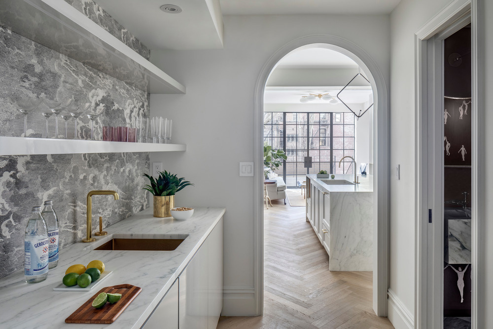 A marble island stretches across the width of this Brooklyn townhouse kitchen, designed for social cooking and framed by steel doors that open to the garden.