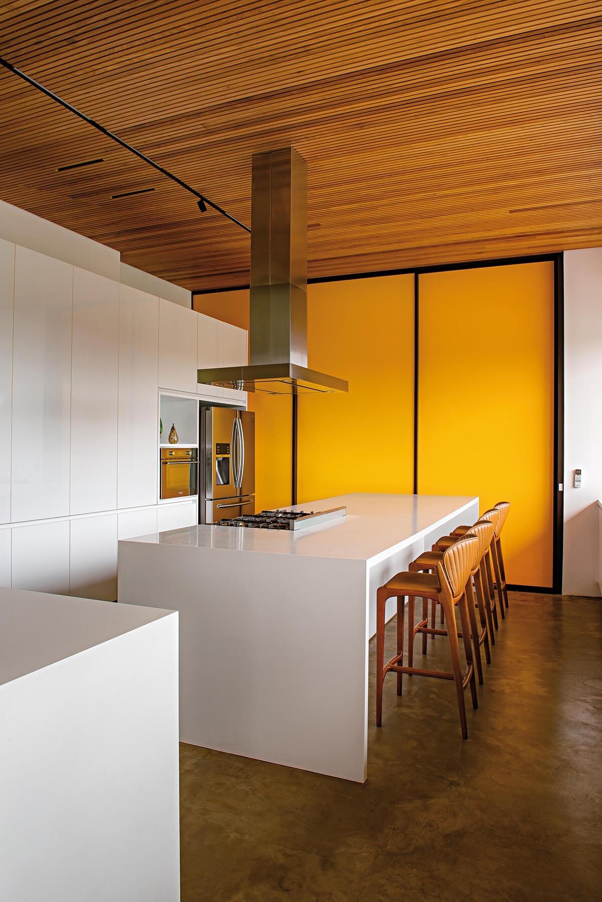 A minimalist white kitchen with handle-free cabinetry, contrasted by a bold yellow accent wall that adds energy and visual impact.