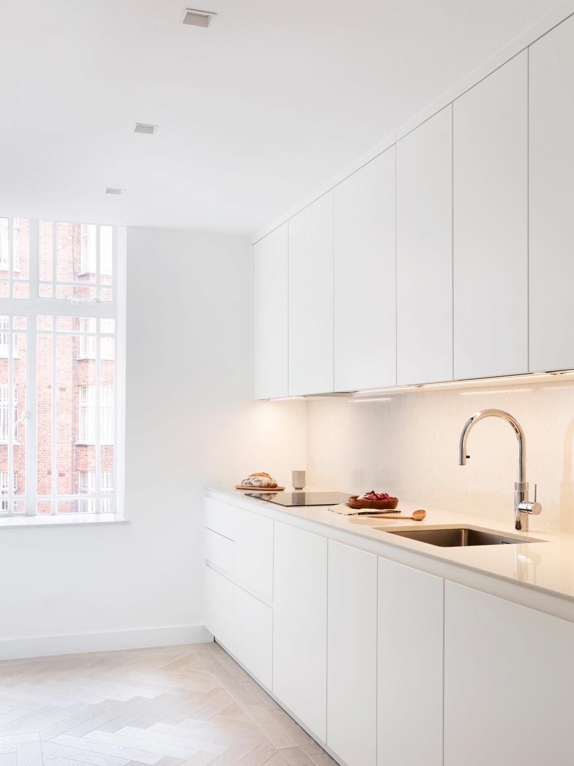 Bright white kitchen with under-cabinet lighting and a full-height window that fills the space with daylight.