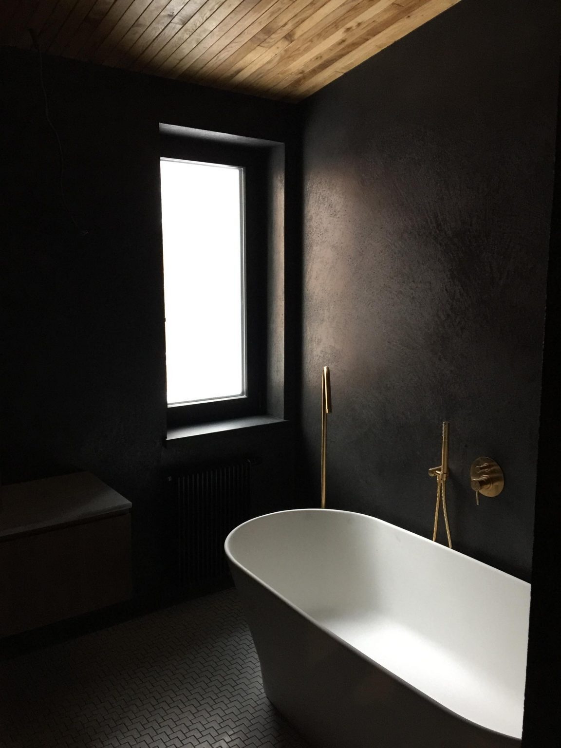 Wood-lined ceilings, doors, and stairs create a warm interior, while a black bathroom with a white bathtub adds a striking visual contrast.