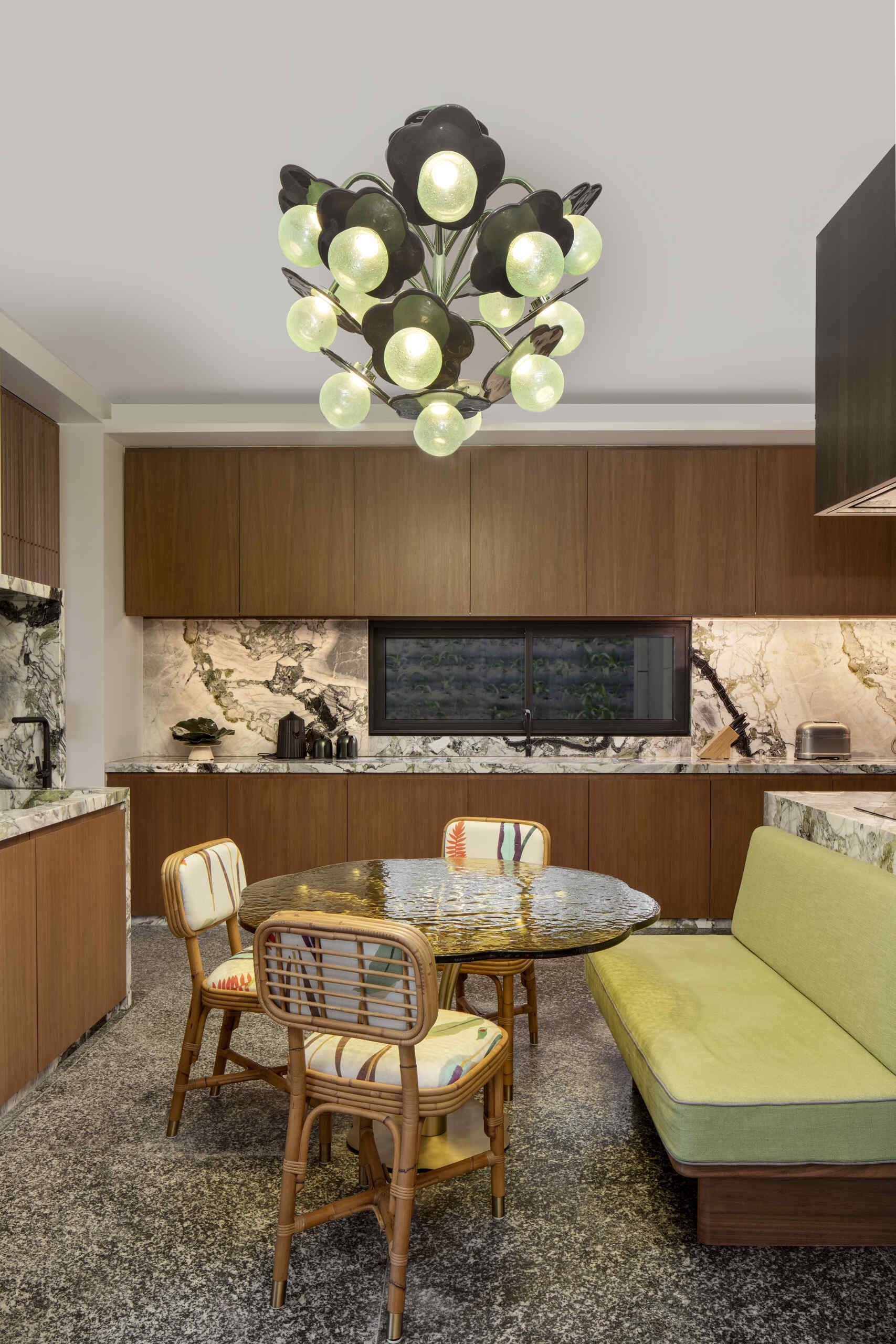 The kitchen follows the same open approach, staying visually connected to the surrounding spaces. A banquette, chairs, and table positioned below a unique lighting fixture introduces a more relaxed dining option.