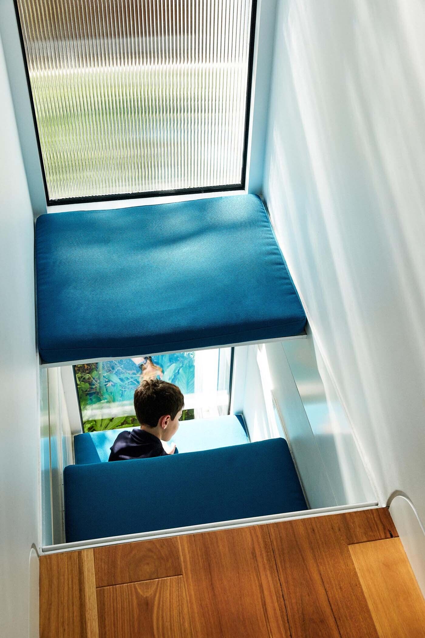 At the end of a hallway, a small seating nook sits beside a window. Upholstered benches make it a comfortable place for children to step away and spend time on their own.
