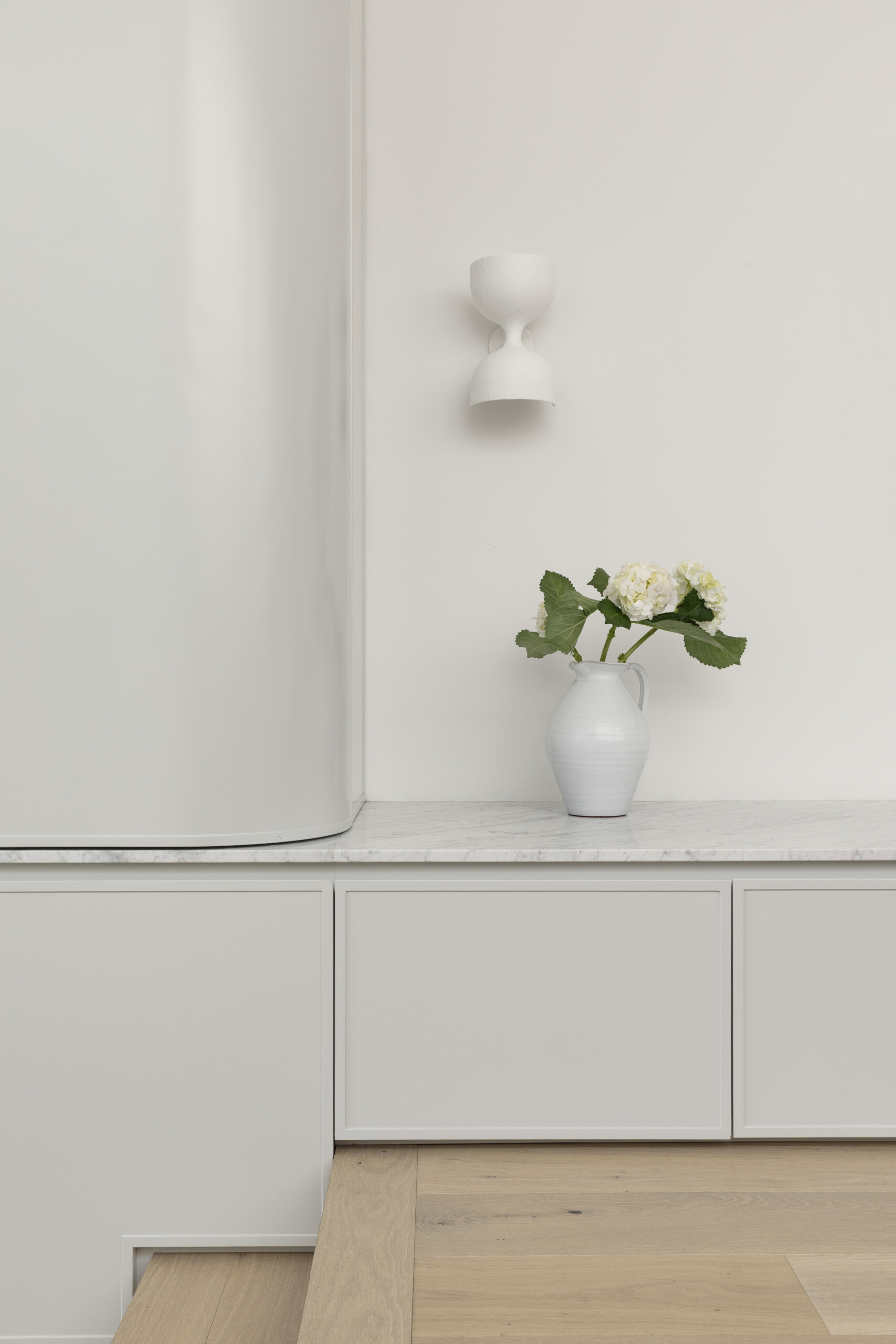 Built-in storage is integrated throughout, keeping the space uncluttered and functional. These elements blend into the architecture, maintaining the clean aesthetic.
A subtle change in level, marked by steps, leads up into the living room, creating a gentle separation without closing off the space.