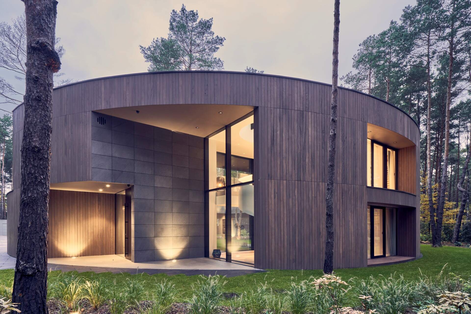 This oval-shaped house uses a continuous frame to wrap functional spaces, creating a bold yet soft architectural presence among the trees.