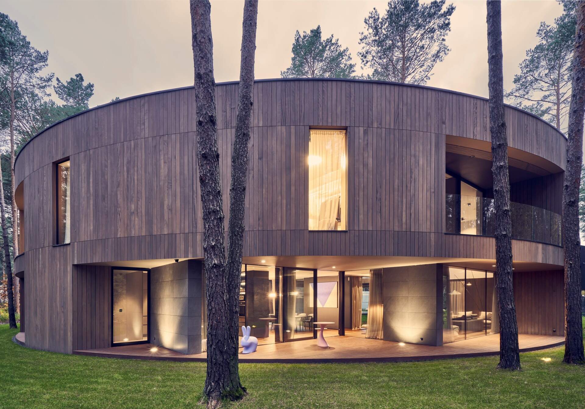 This oval-shaped house uses a continuous frame to wrap functional spaces, creating a bold yet soft architectural presence among the trees.