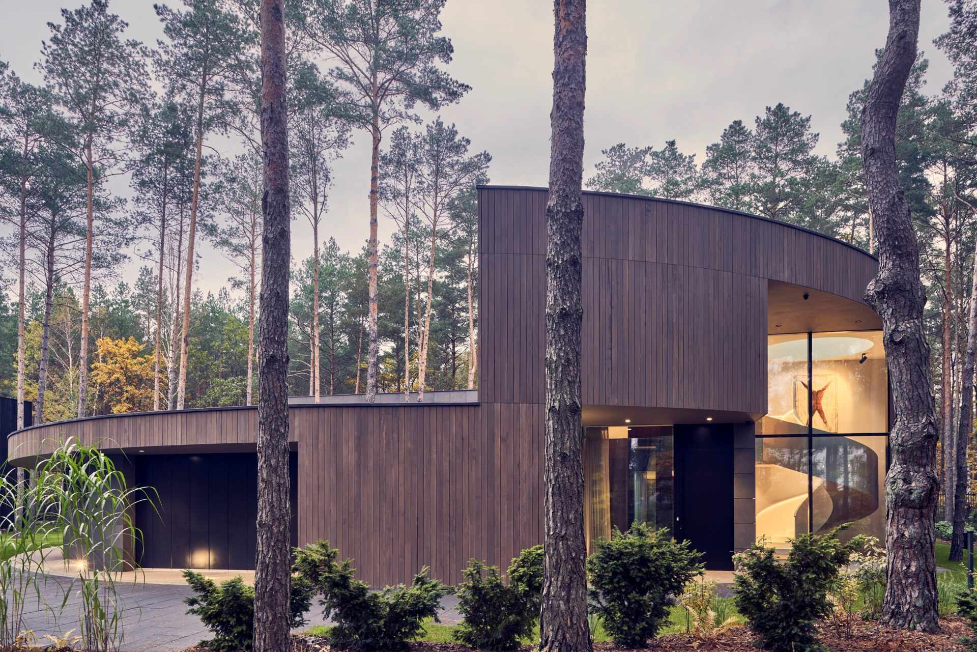 This oval-shaped house uses a continuous frame to wrap functional spaces, creating a bold yet soft architectural presence among the trees.