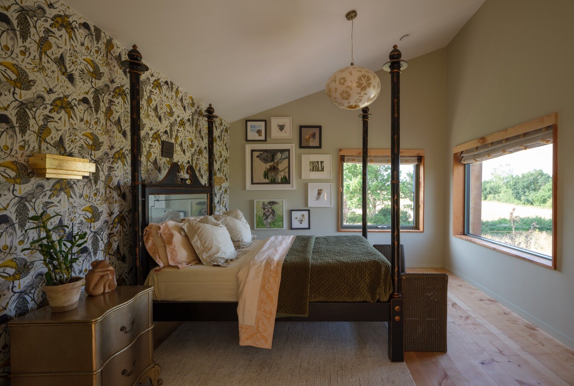 The bedroom, with its angled ceiling and wood window trim, features a nature-inspired wallpaper accent wall that adds just enough color and complements the overall tone of the room.