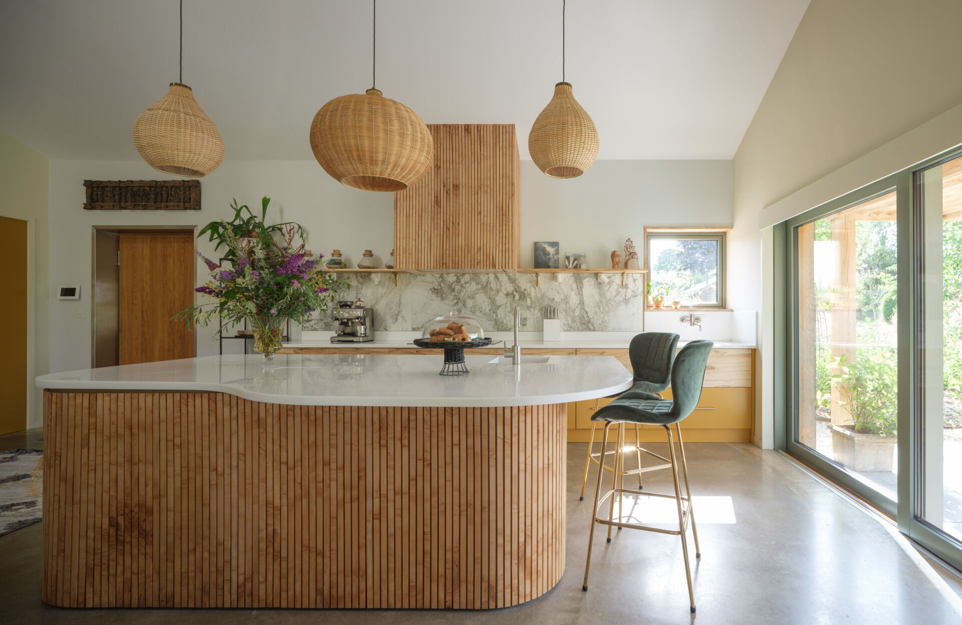 A curved timber island, marble backsplash and woven pendants create a warm, light-filled kitchen with direct access to the garden.
