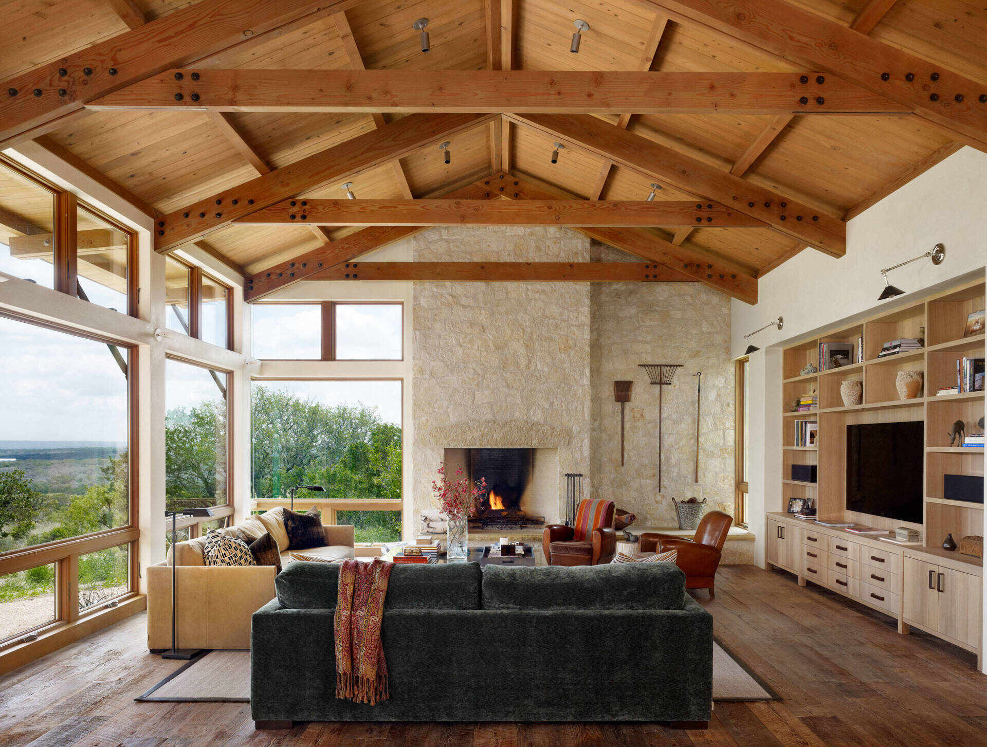 A living room where limestone walls meet exposed wood trusses, creating a warm and textured interior anchored by a stone fireplace.